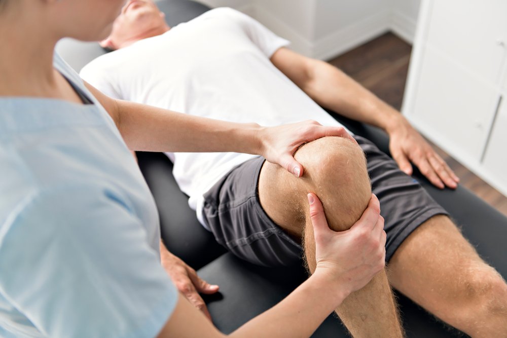 A person receiving knee physical therapy or examination from a healthcare professional in a clinical setting.