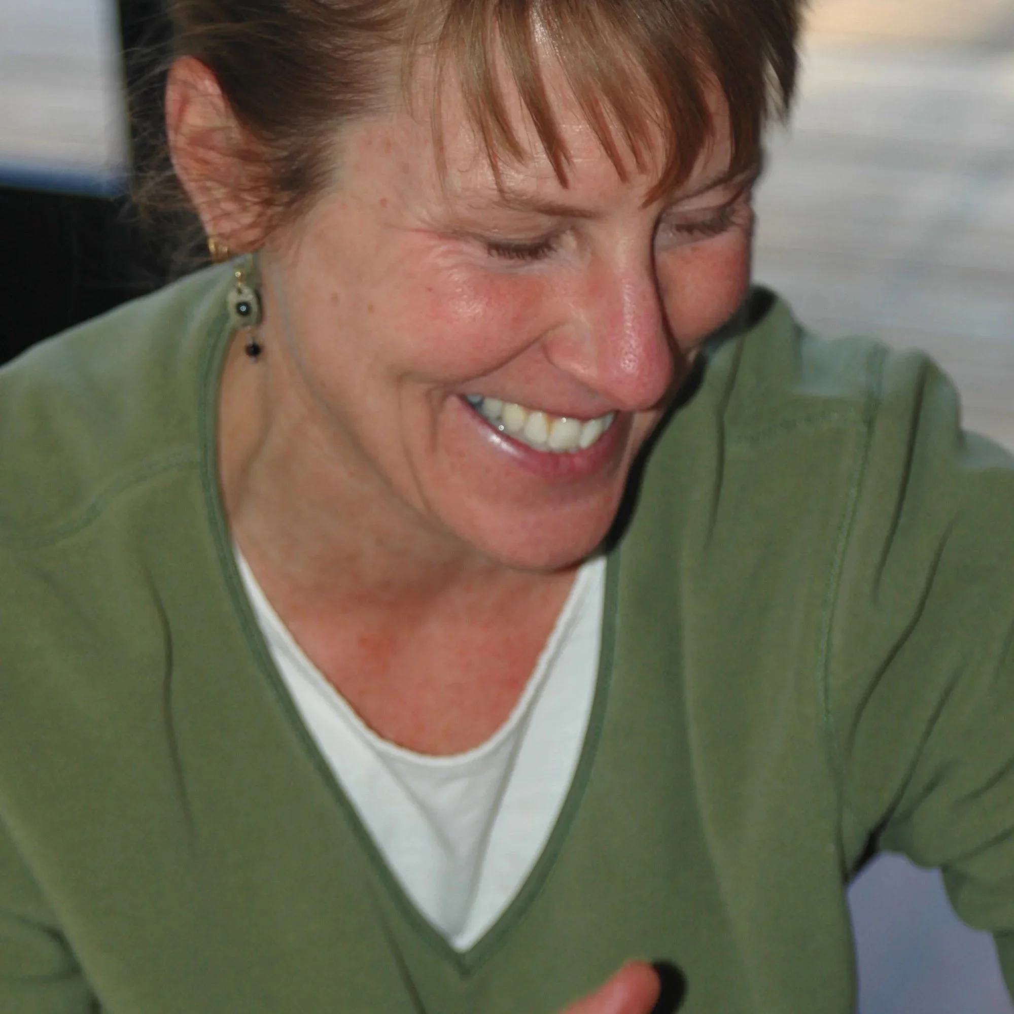 Close-up of a smiling woman with short red hair wearing a green sweater and earrings, looking down.