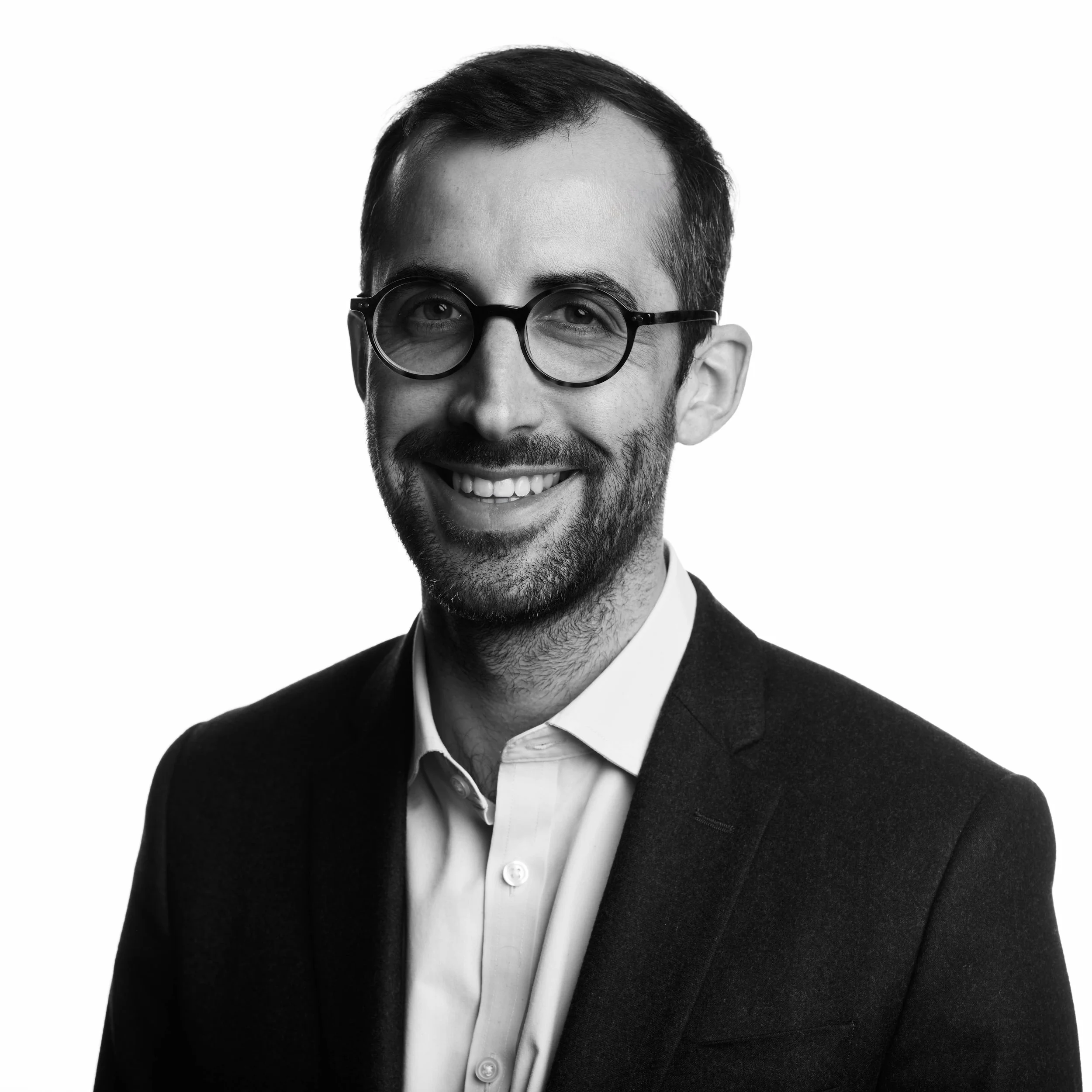 Black and white portrait of a man with dark hair, glasses, and a beard, smiling, wearing a tuxedo with a white shirt and a bow tie.