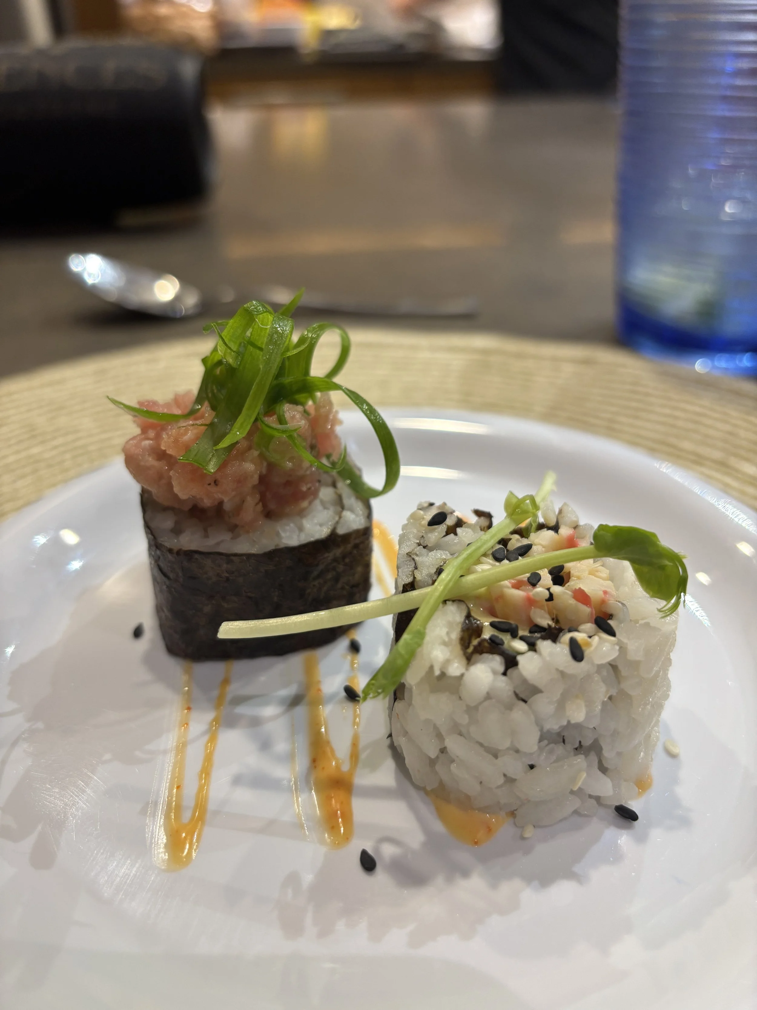 Two yellowfin sushi rolls , garnished with green onions and a drizzle of sriracha cream.