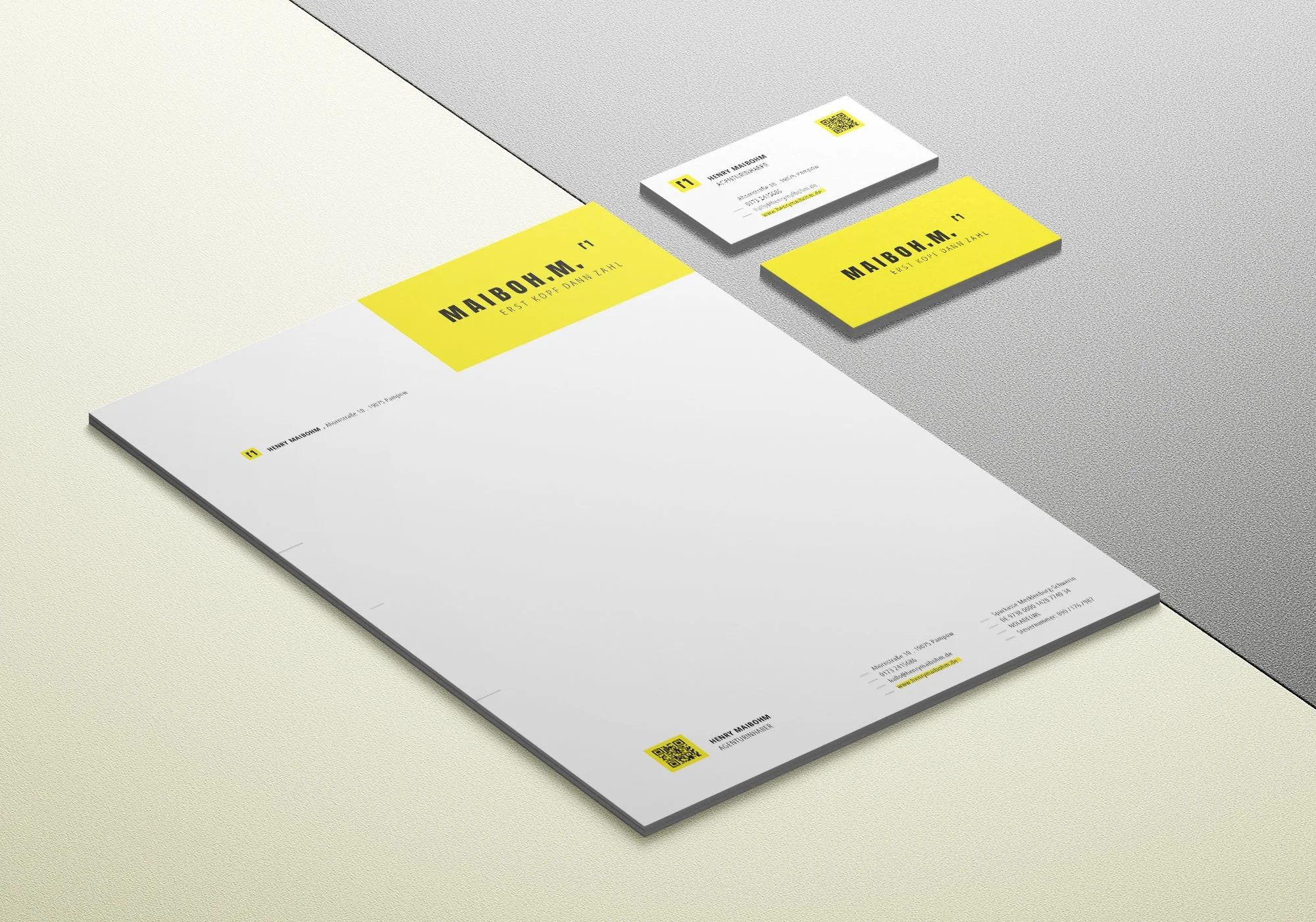 Visitenkarte, Briefpapier und Briefumschlag mit gelben Akzenten und QR-Codes auf einer grauen und hellen Oberfläche. Das Design enthält den Namen Henry Maibohm, Kontaktdaten und den Slogan "Erst Kopf, dann Zahl".