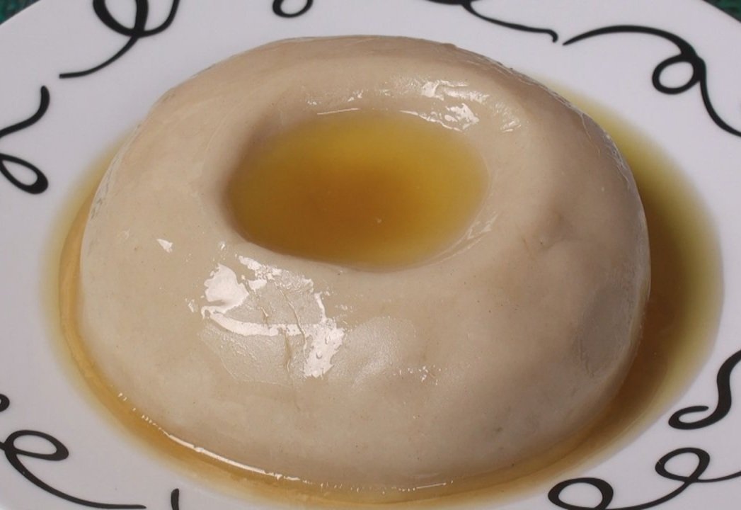 A white, round dessert with a hole in the center, topped with caramel sauce, served on a decorative plate