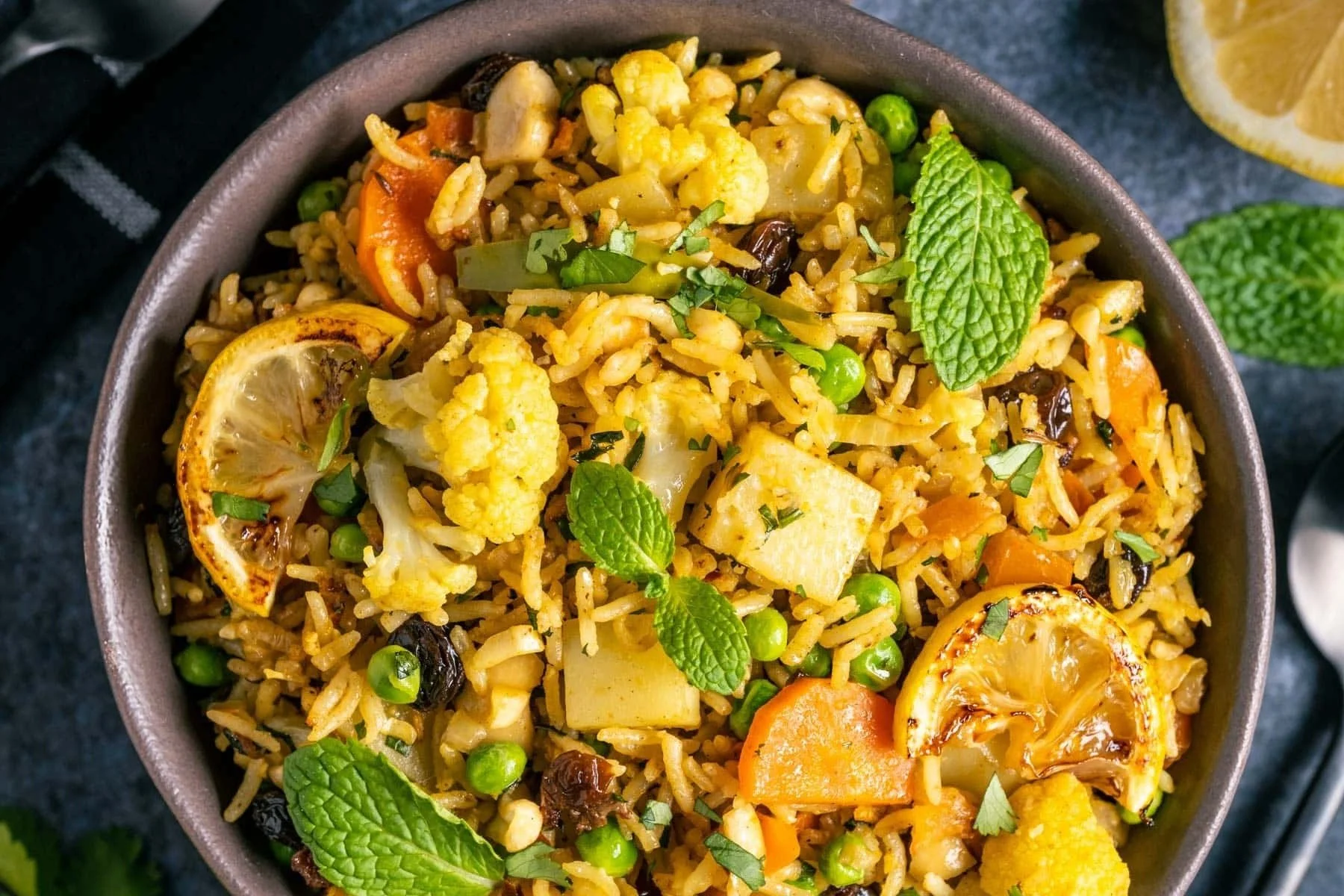 Bowl of vegetable fried rice with cauliflower, carrots, green peas, lemon slices, and fresh mint leaves.