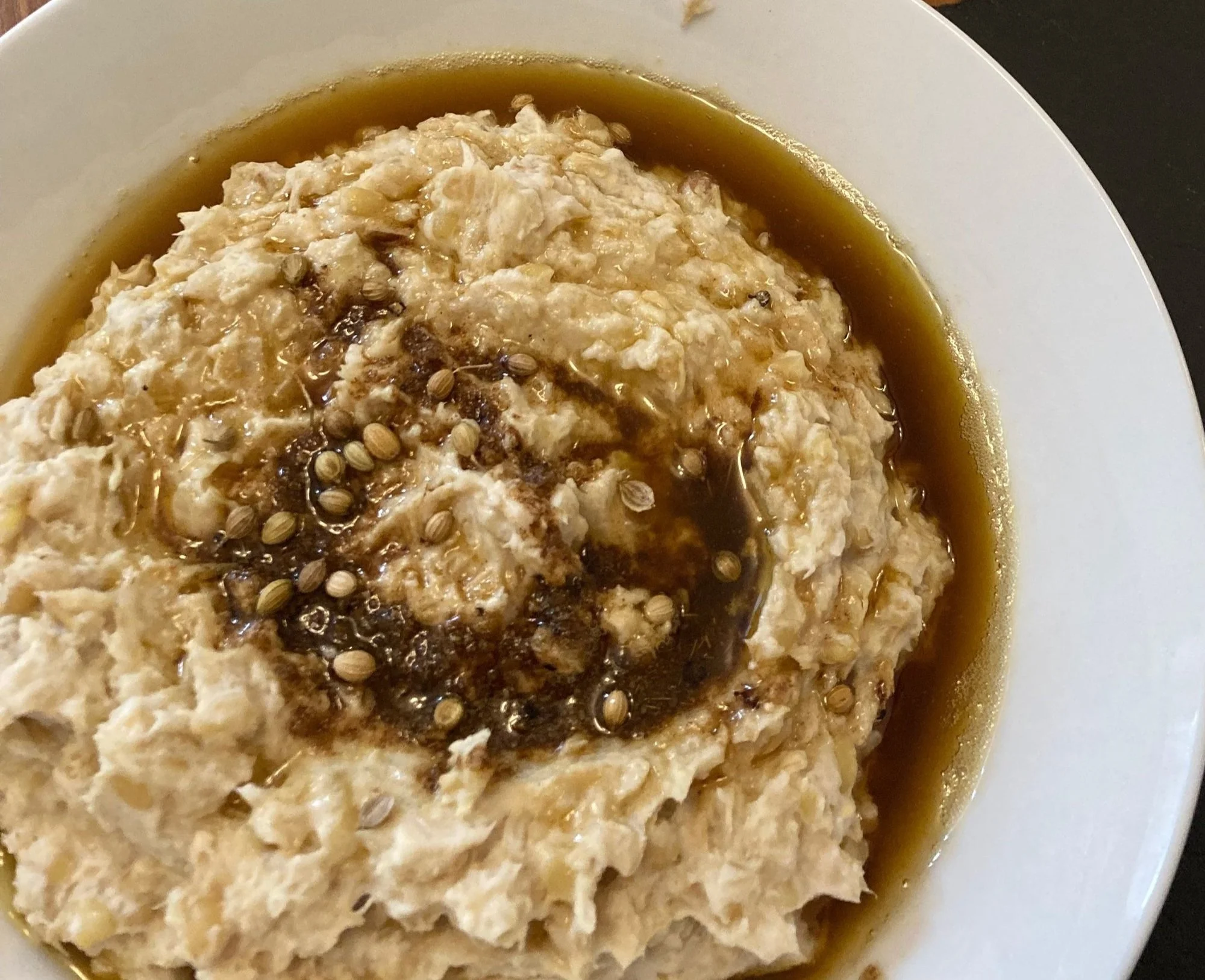 A bowl of oatmeal topped with seeds, syrup, and spices, with a side of brown sauce or syrup around the edges.