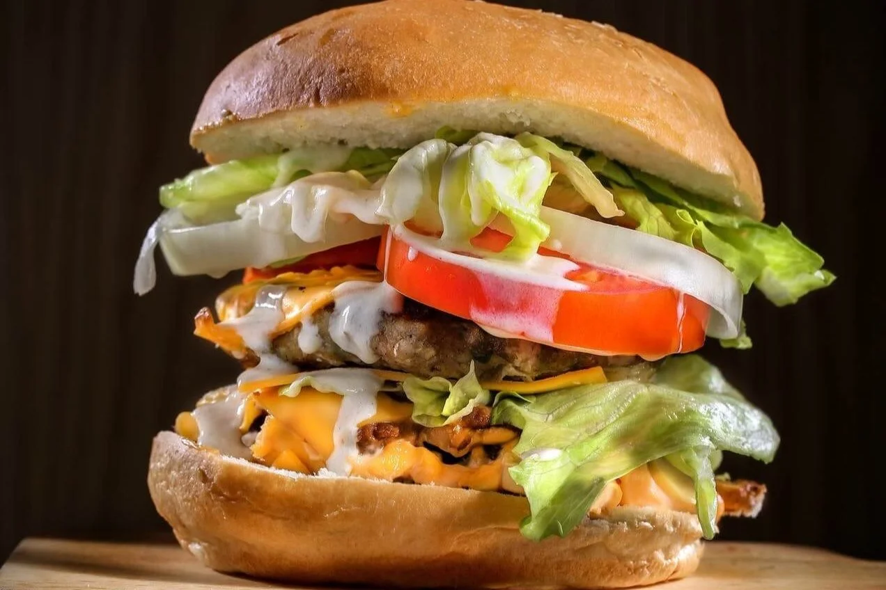 Close-up of a large cheeseburger with lettuce, tomato, onion, cheese, a patty, and a sandwich bun on a wooden surface.