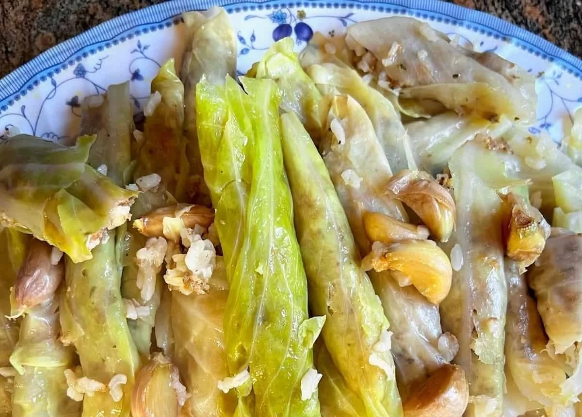 Close-up of cooked lettuce with garlic, rice, and oil on a decorative blue and white plate.