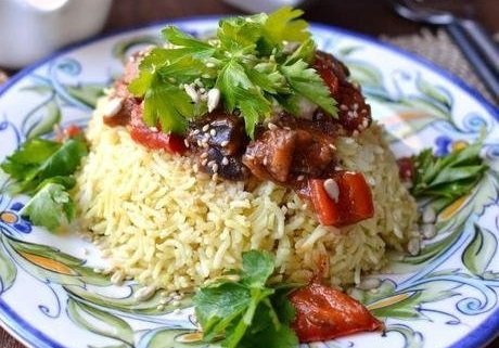 Plate of rice topped with grilled vegetables, and fresh cilantro on a decorative plate.