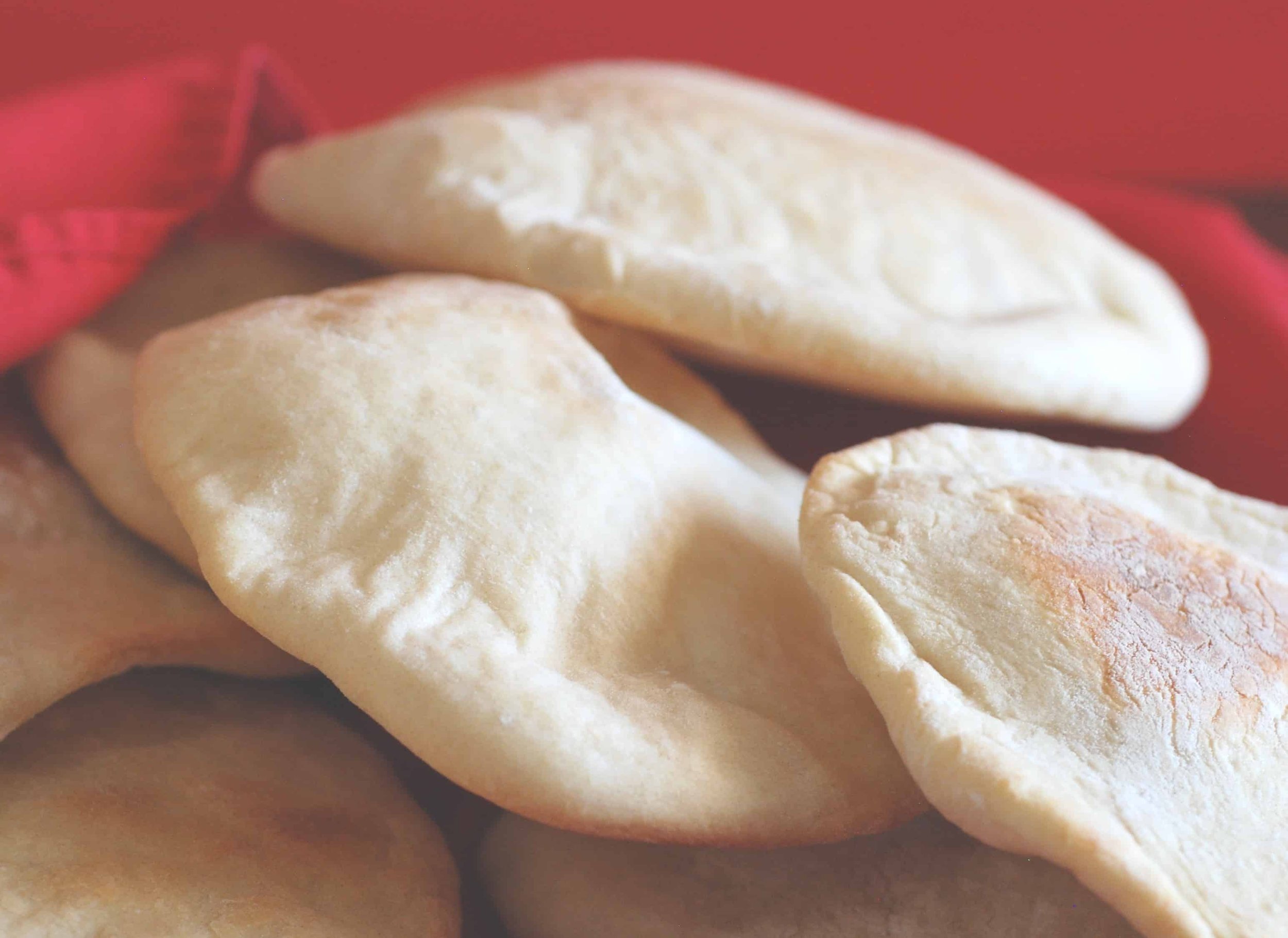 Close-up of freshly baked flatbread or pita bread stacked on top of each other with a red cloth in the background.