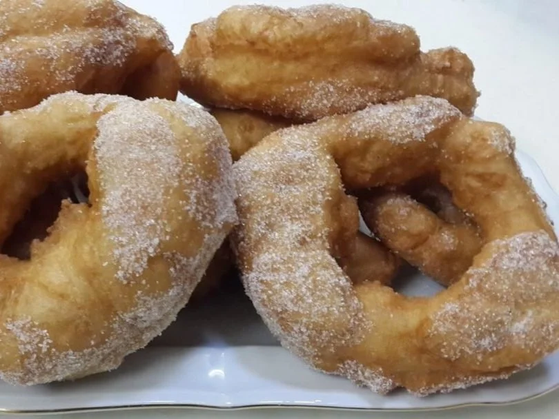 A plate of sugar-coated glazed donuts arranged on a white dish.