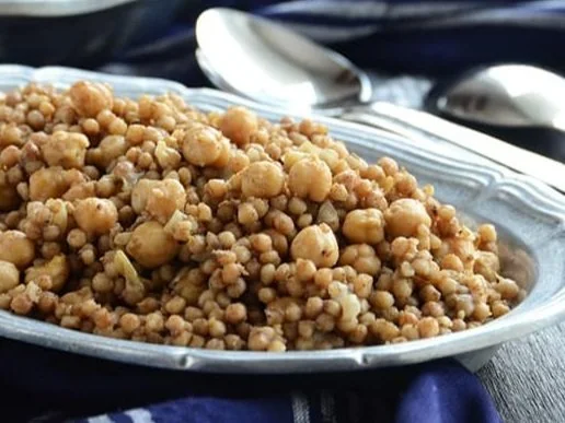 A silver serving dish filled with cooked chickpeas and bulgur, served on a dark blue tablecloth with spoons nearby.