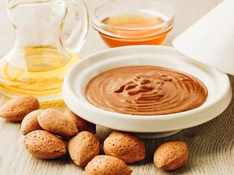 Chocolate pudding in a white bowl with walnuts, honey, and cream nearby.