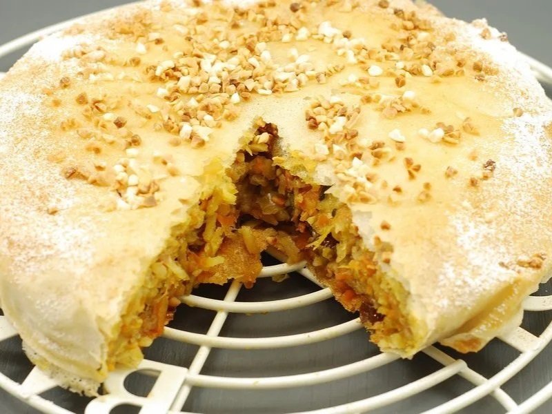 A sliced apple pie with a golden crust, sprinkled with chopped nuts on top, resting on a cooling rack.