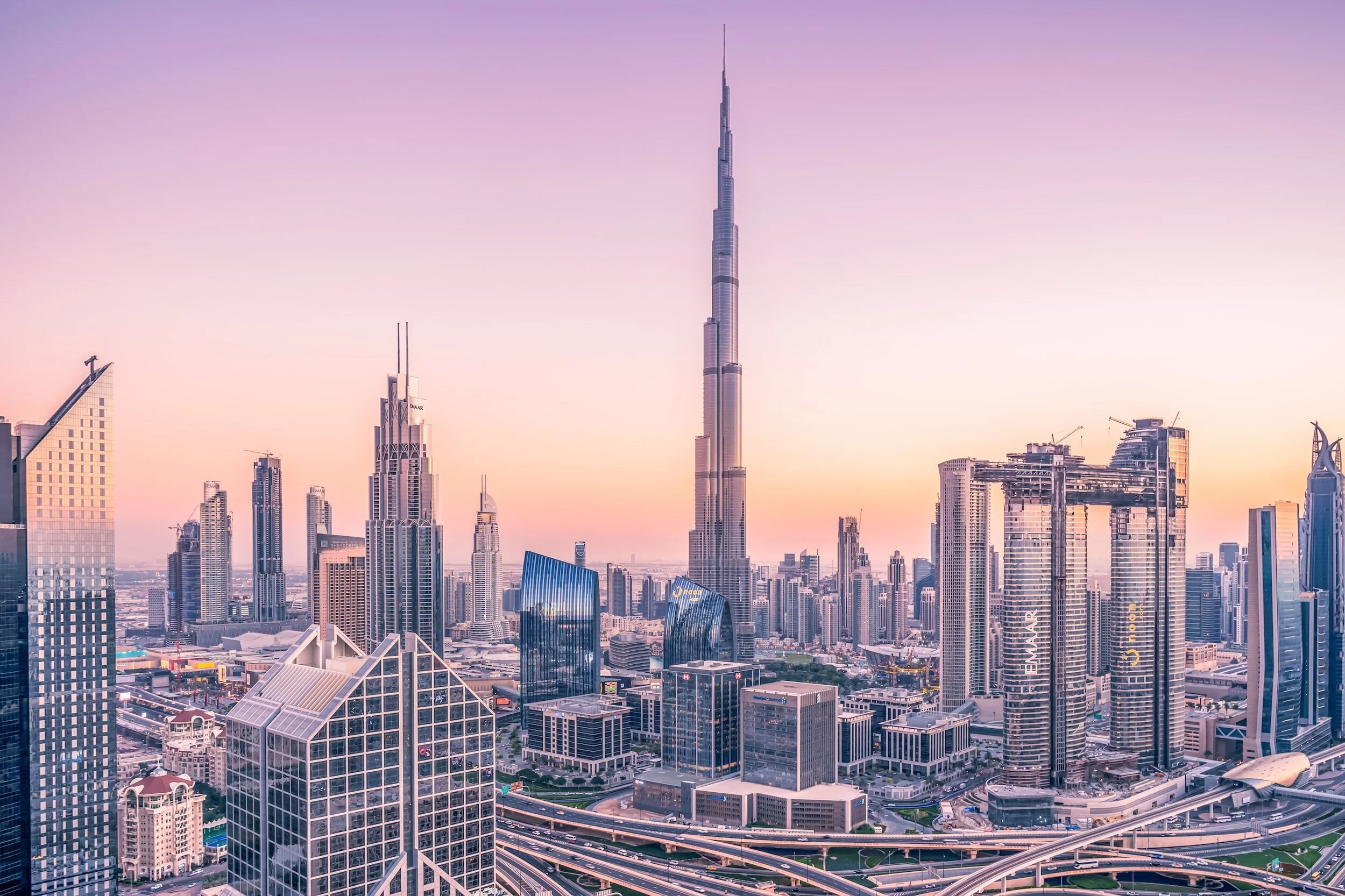 Sunset view of downtown Dubai skyline with the Burj Khalifa at the center, surrounded by modern skyscrapers and city roads.