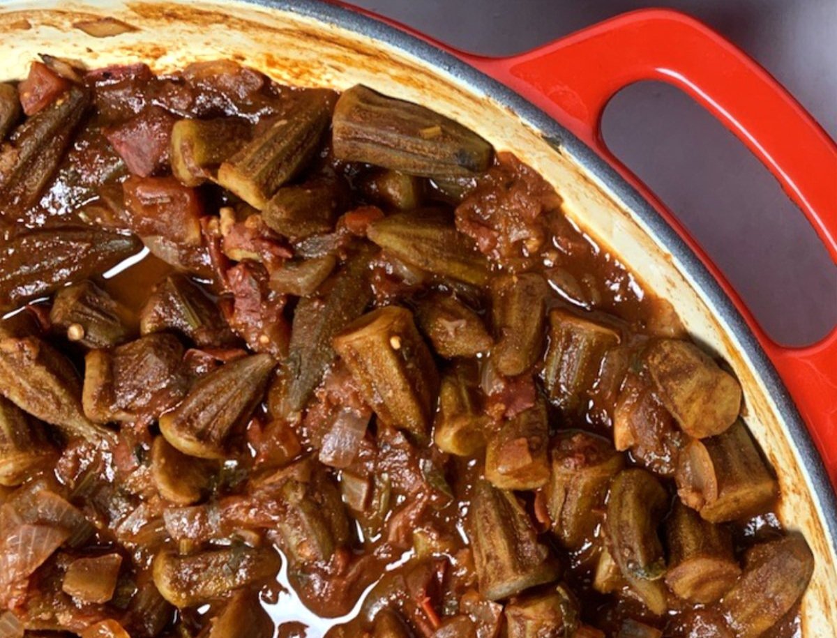 Cooked okra and meat in a red skillet with tomato-based sauce