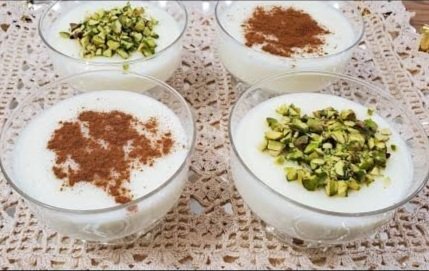 Four bowls of dessert with chopped pistachios and cinnamon on top, placed on a lace tablecloth.