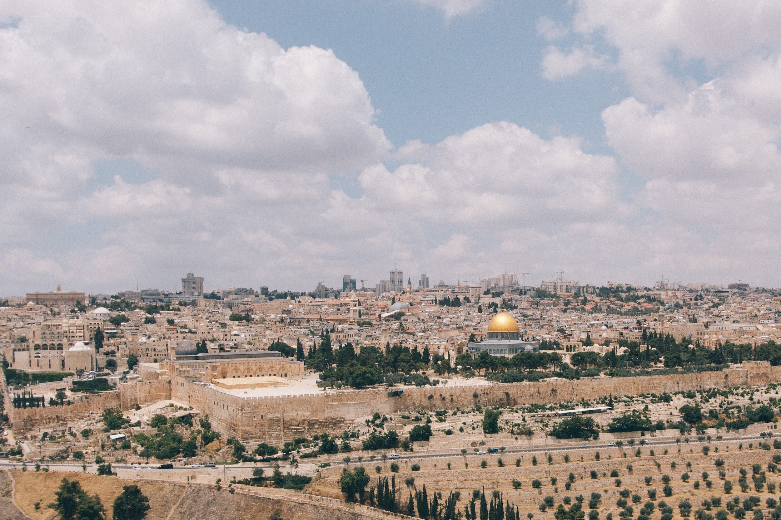 A panoramic view of Jerusalem with a clear sky, featuring the golden Dome of the Rock and surrounding historic buildings and cityscape.