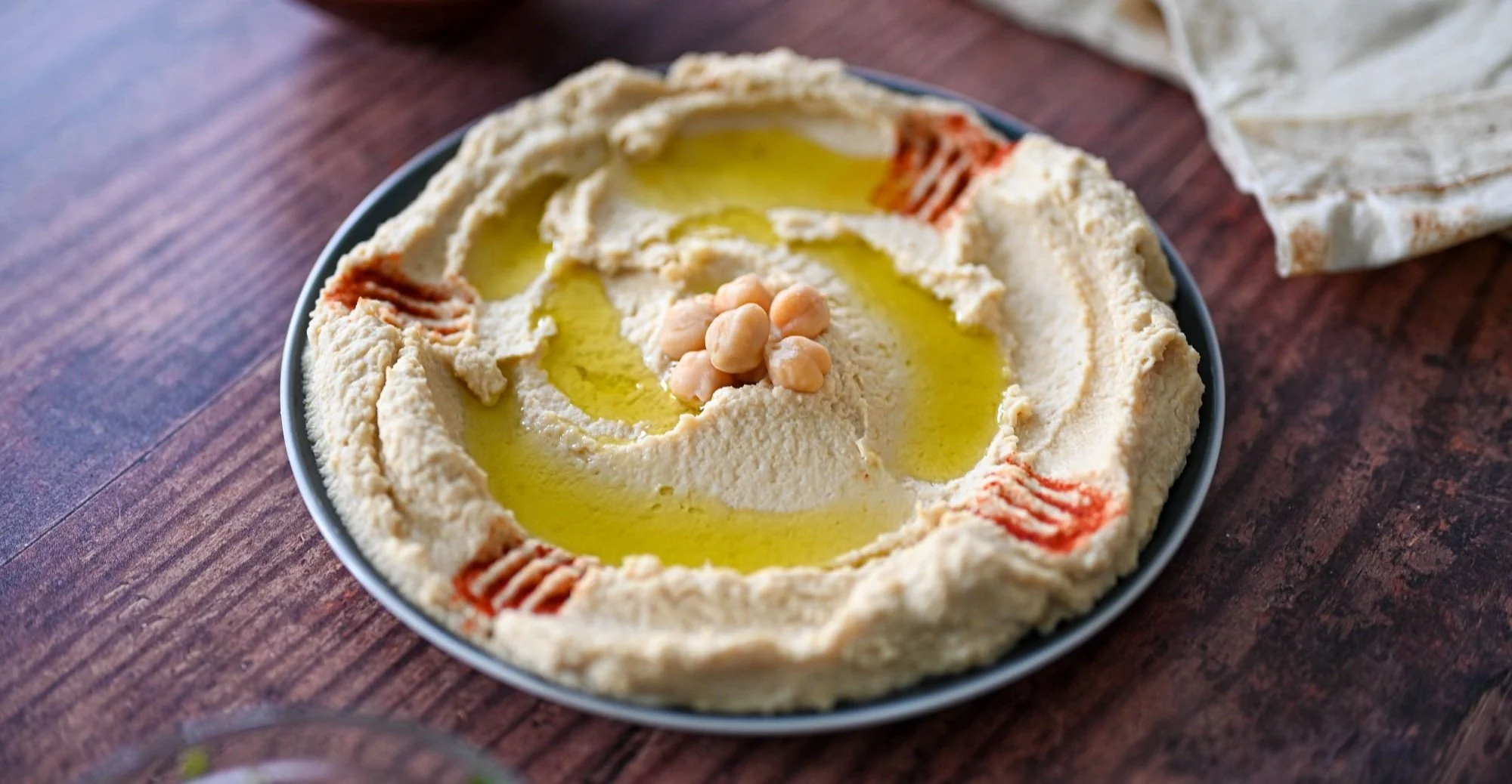 A plate of hummus topped with chickpeas, olive oil, and paprika on a wooden table.