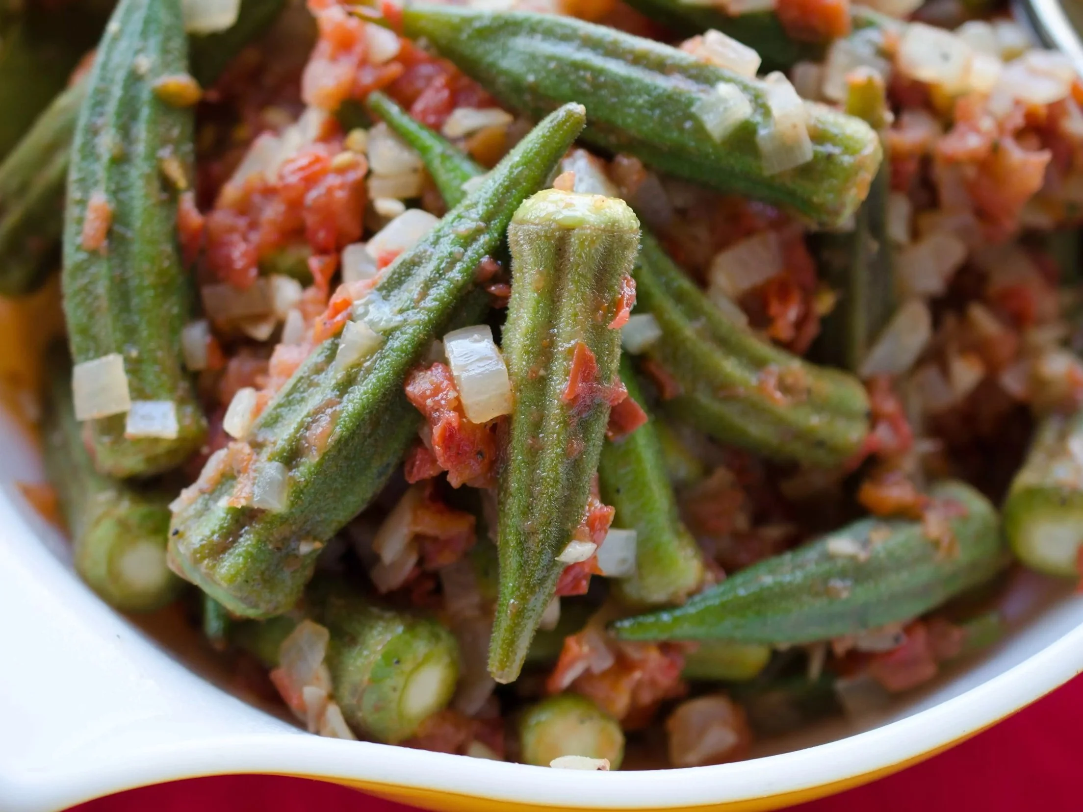 Close-up of cooked okra with chopped onions and tomatoes in a white dish.