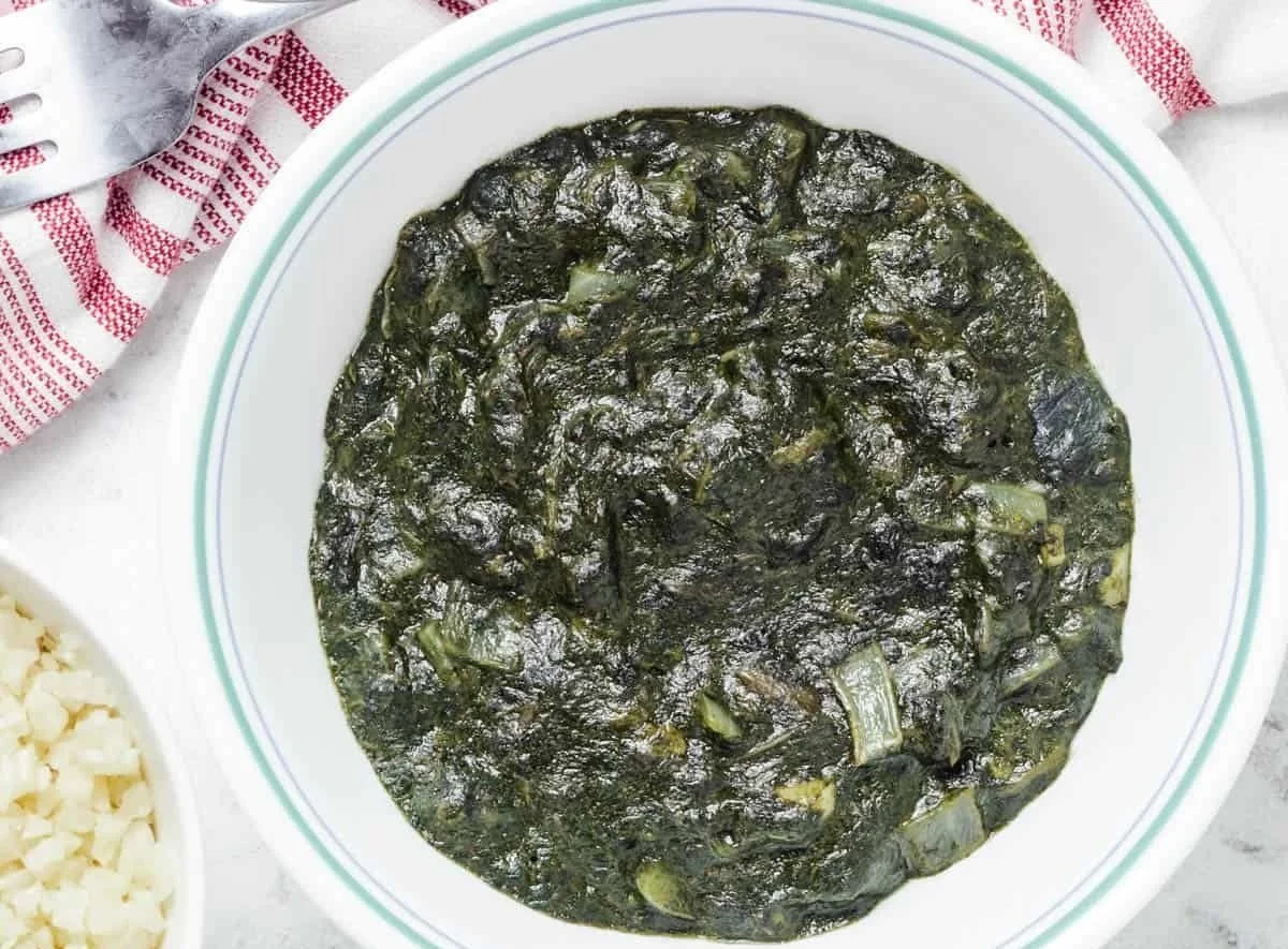 A bowl of cooked greens, possibly collard greens or spinach, in a white bowl with green stripes.