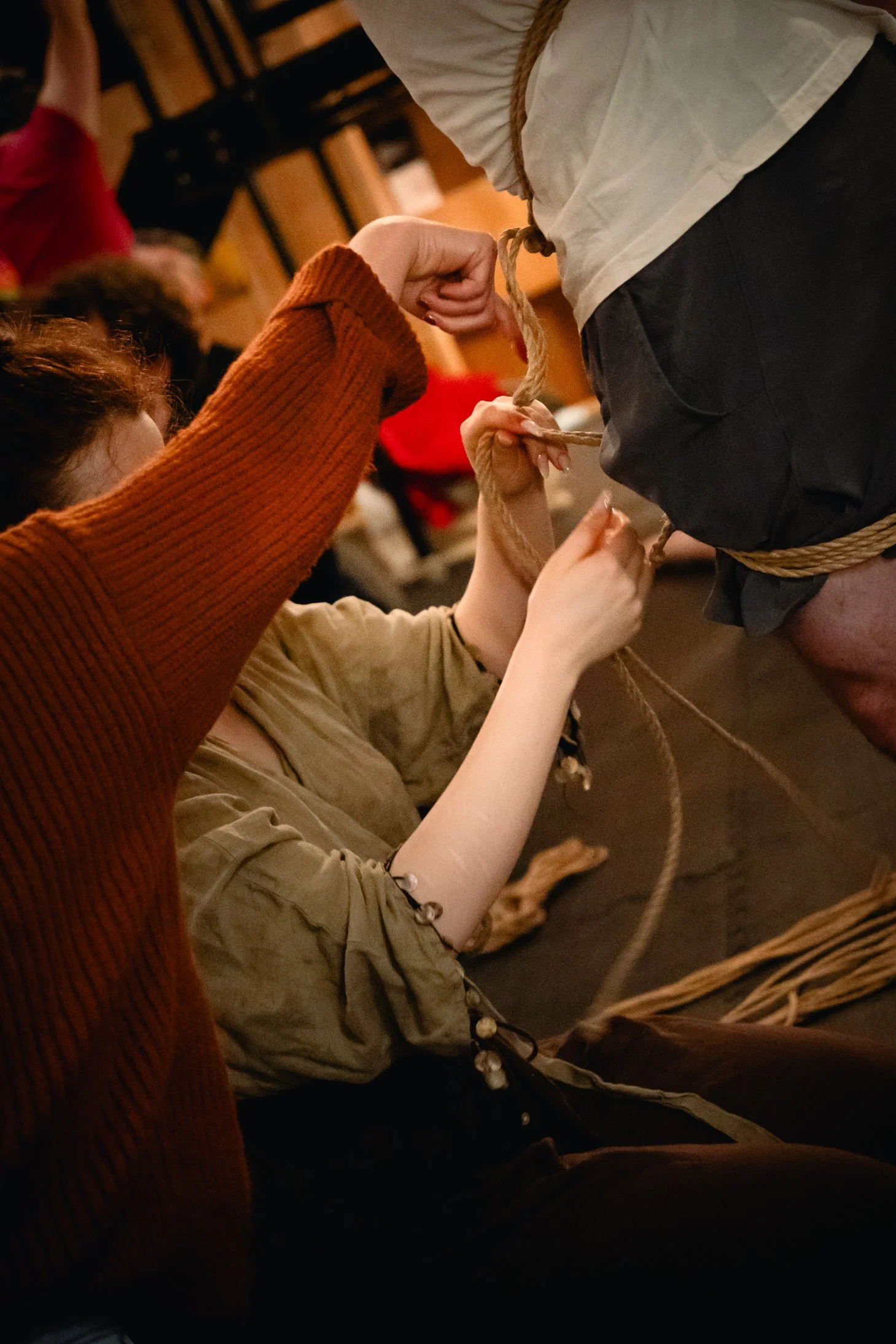 Two people tying up a man with rope in a dimly lit room, possibly during a performance or reenactment.