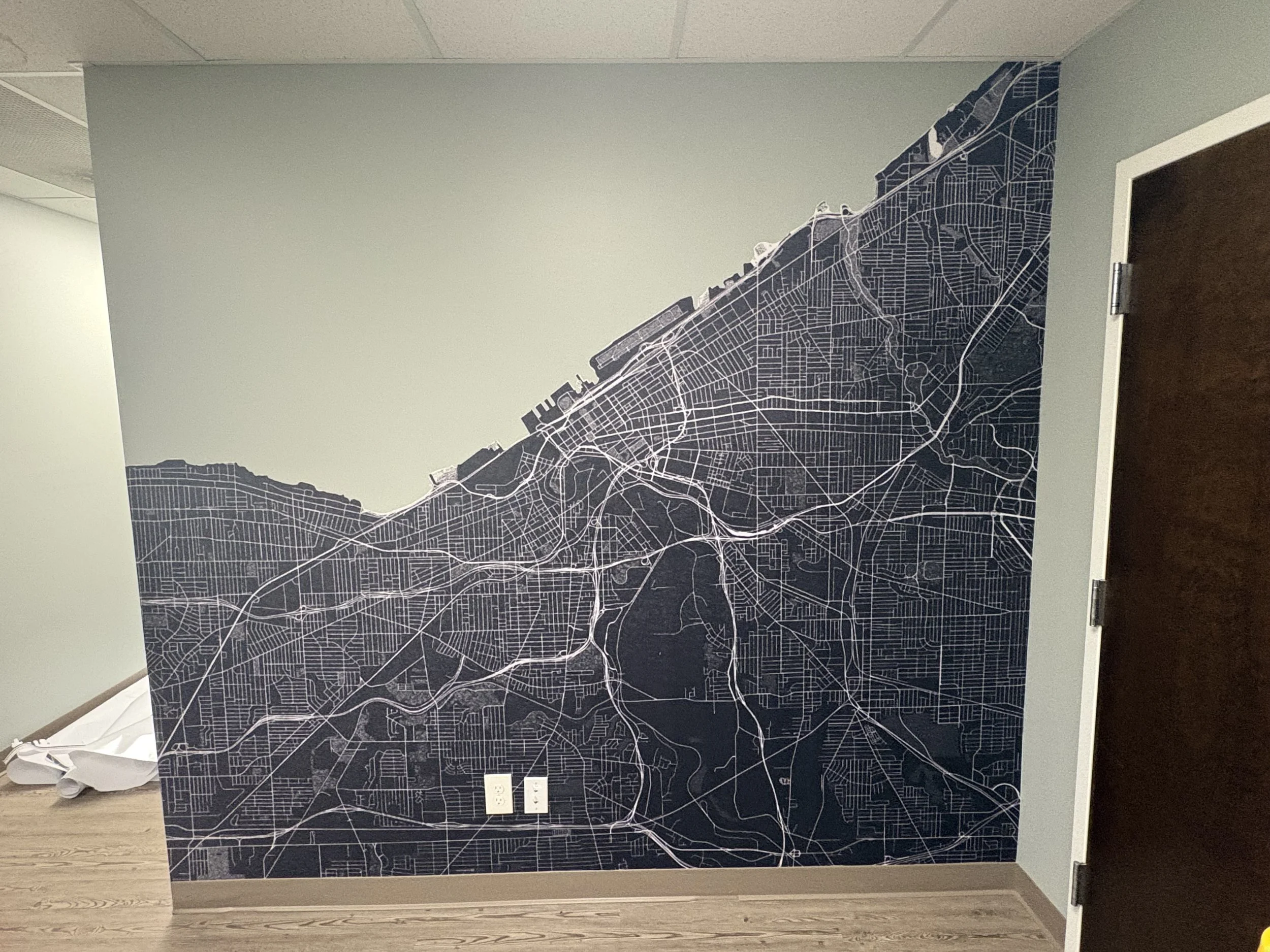 Interior wall decorated with a large map of a city in dark colors, featuring streets and highways, located in an indoor office or conference room with electrical outlets at the bottom.
