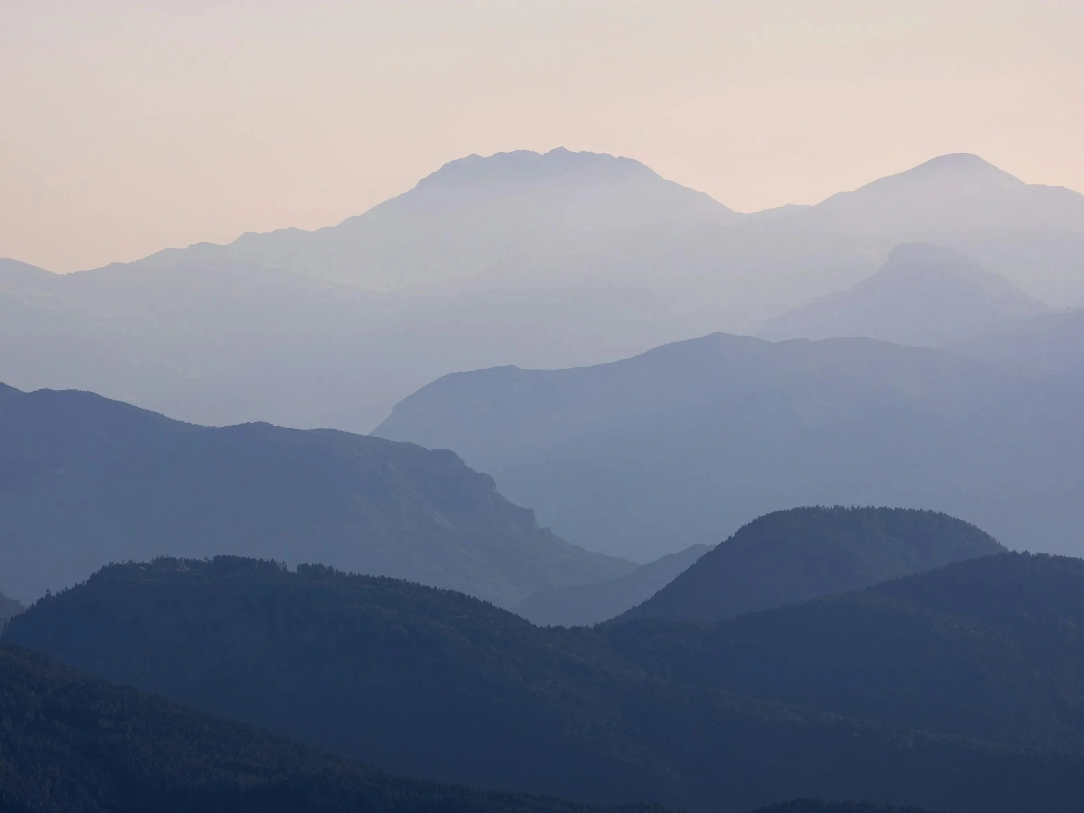 Blaue und graue Bergketten bei Sonnenaufgang oder Sonnenuntergang, in der Ferne Nebel oder Dunst zwischen den Bergen.