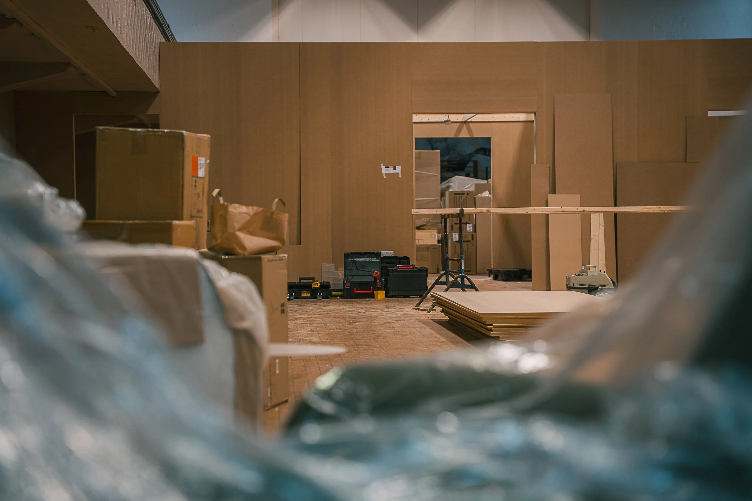  Interior of a room under construction with cardboard boxes, tools, and wooden panels scattered around.