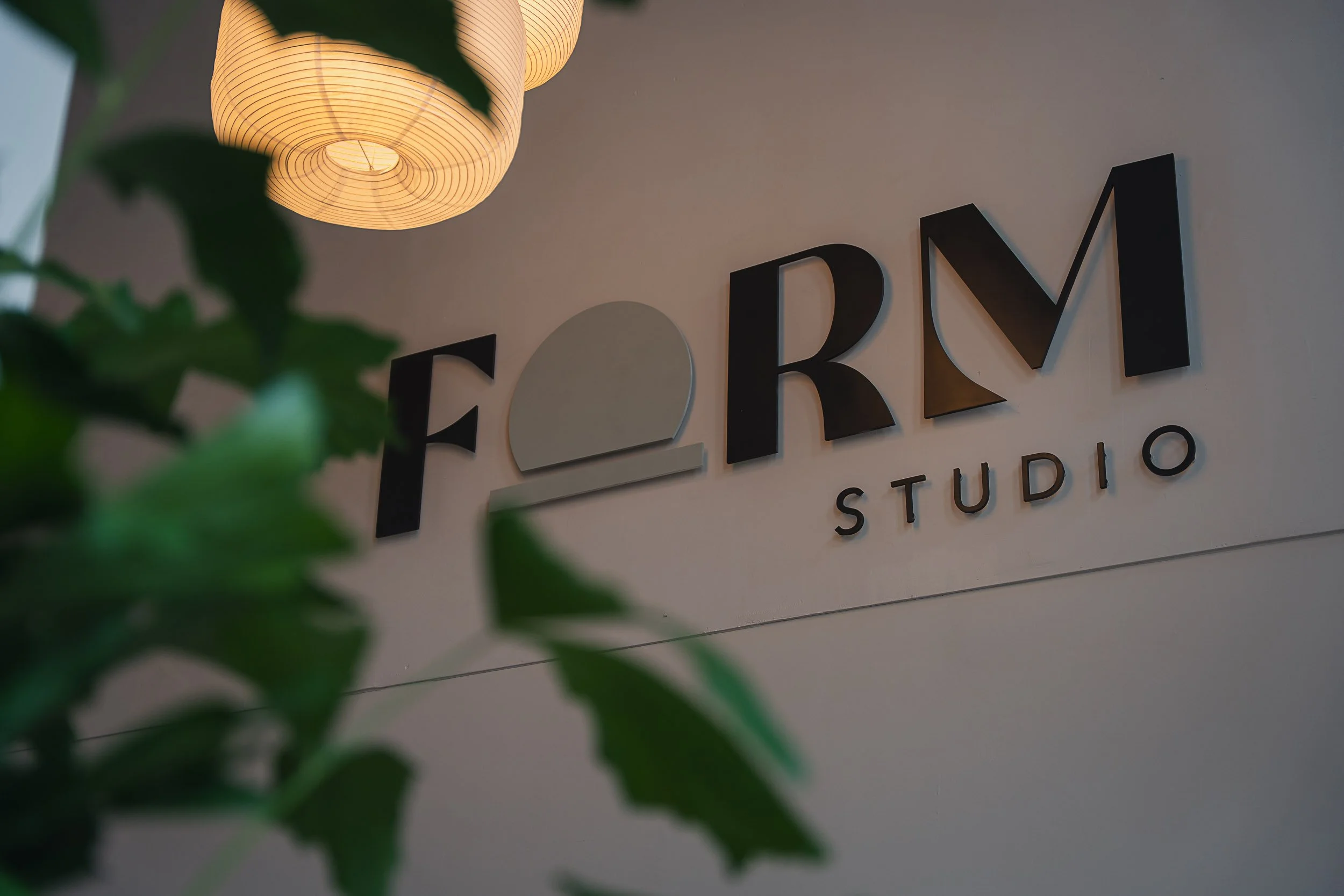 Sign reading 'FARM STUDIO' with a leaf in the foreground and a hanging paper lantern overhead.