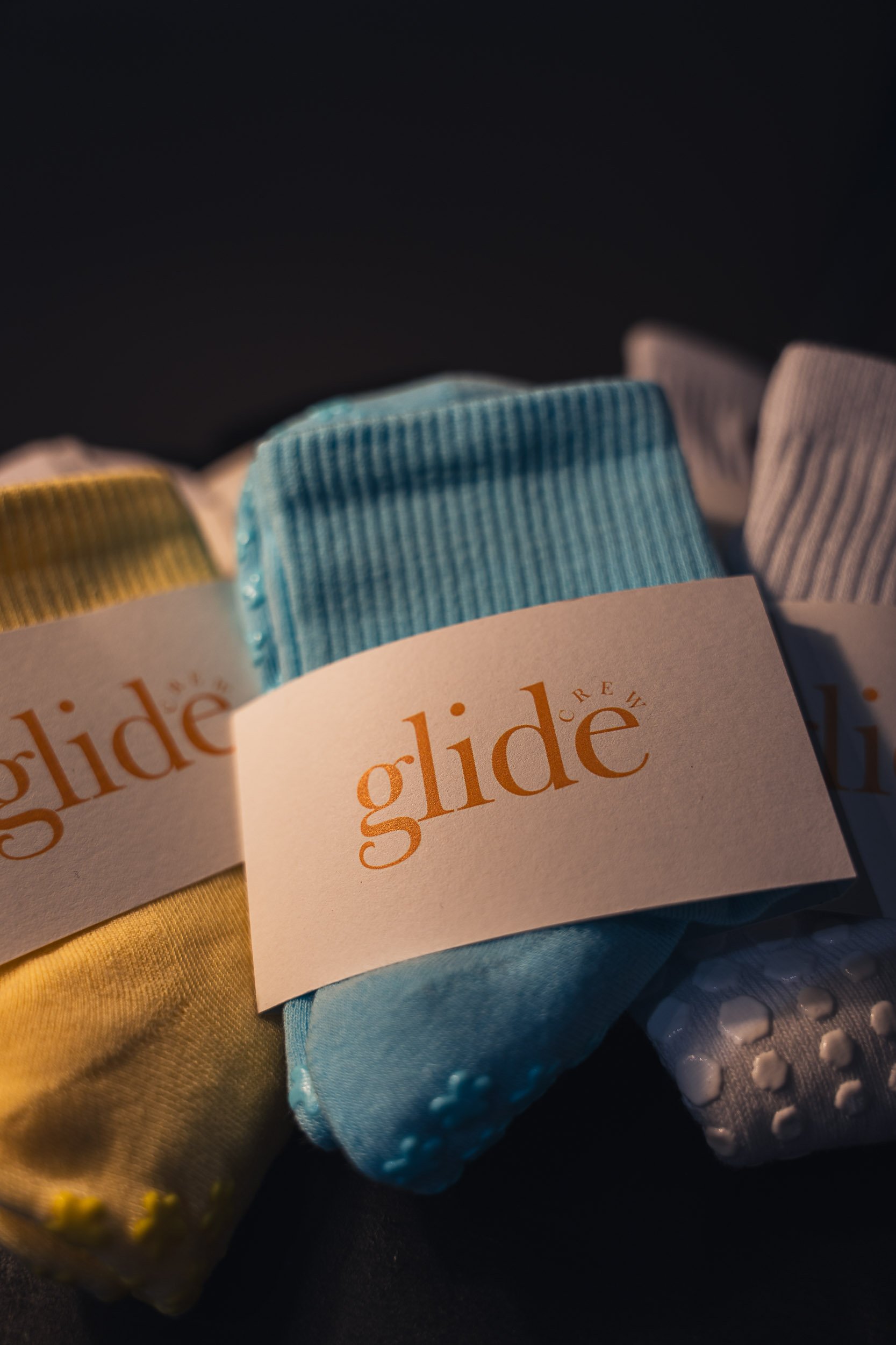 Three pairs of colorful socks with branded labels, in yellow, blue, and gray colors, on a dark background.