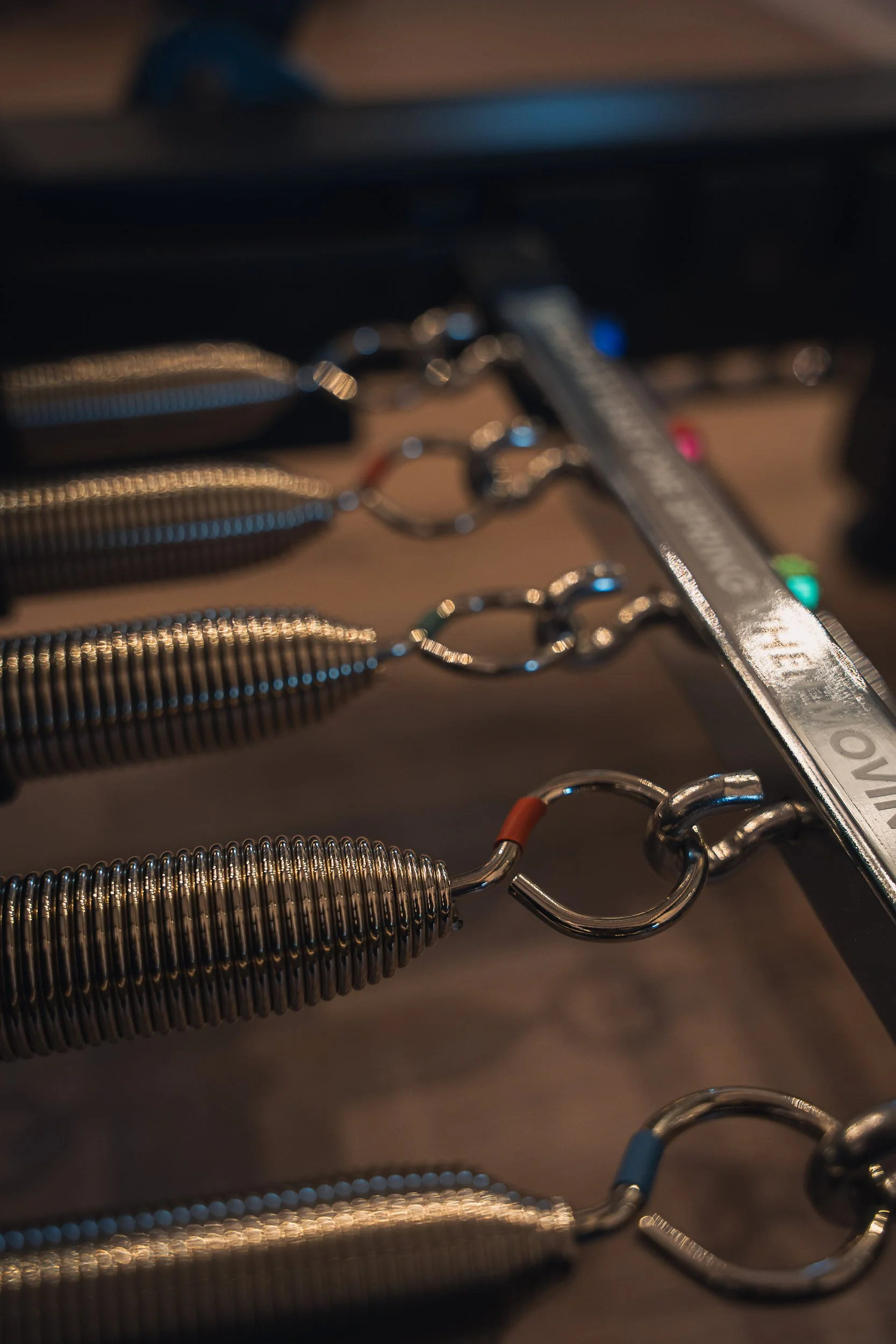 Close-up of metallic hooks attached to coiled springs, arranged in a row on a wooden surface with a metal ruler nearby.