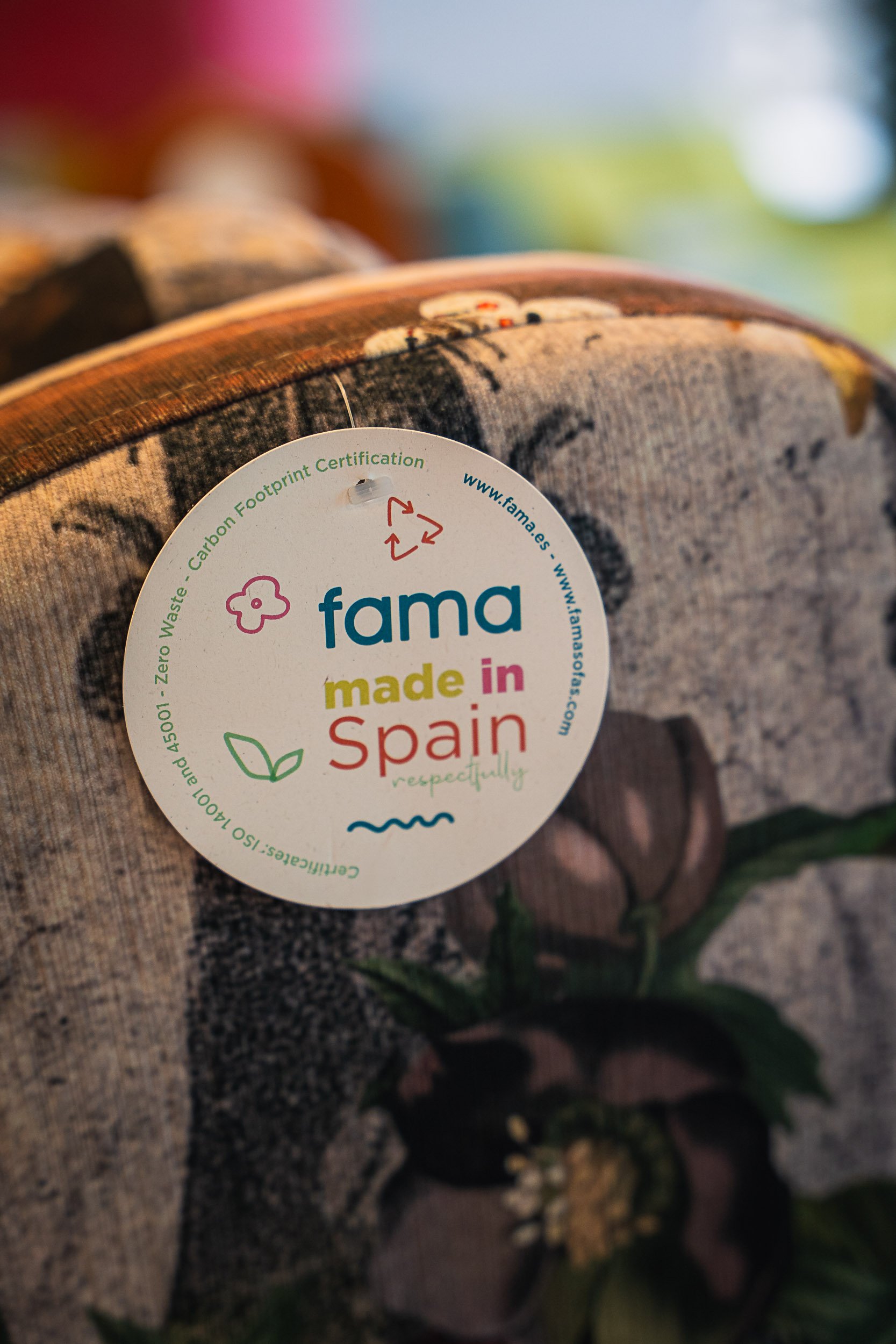 A circular label attached to a fabric object, indicating it is made in Spain with eco-friendly certification and recyclable symbols.
