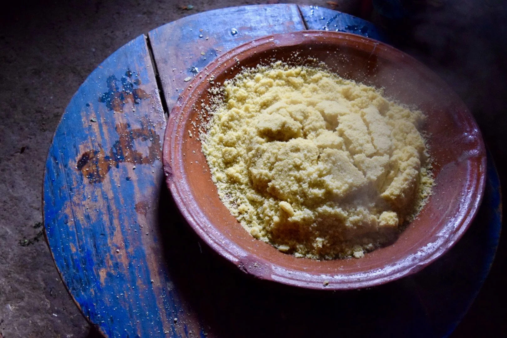 A bowl of yellowish flour on a blue wooden table.