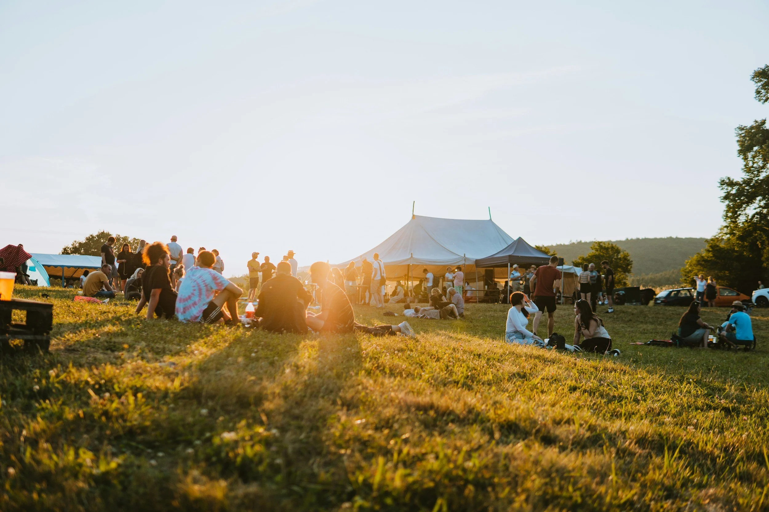 A woman and a young girl are playing Jenga outdoors on a grassy field, with other people standing in line or watching in the background.