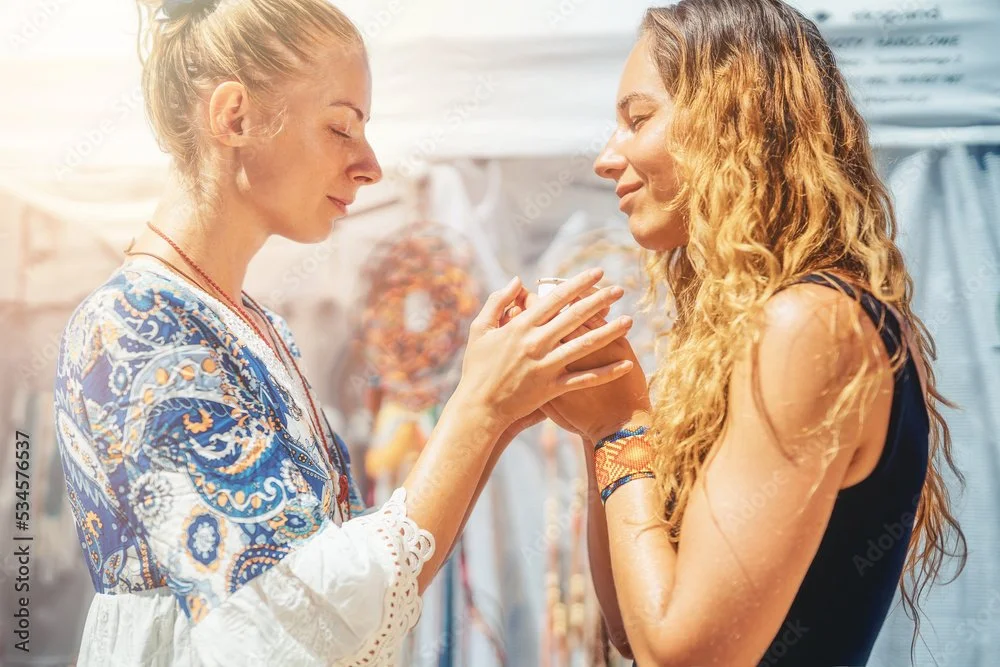 Two women sharing a moment, one offering an item to the other in a bright, colorful setting.