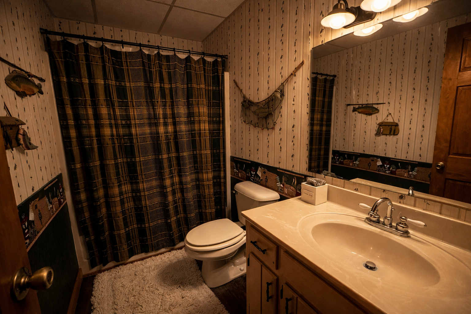 A rustic bathroom with wood-paneled walls, plaid curtains, fish-themed wall decorations, a mirror, a cream-colored countertop with a sink, and a toilet, illuminated by a multi-bulb light fixture.