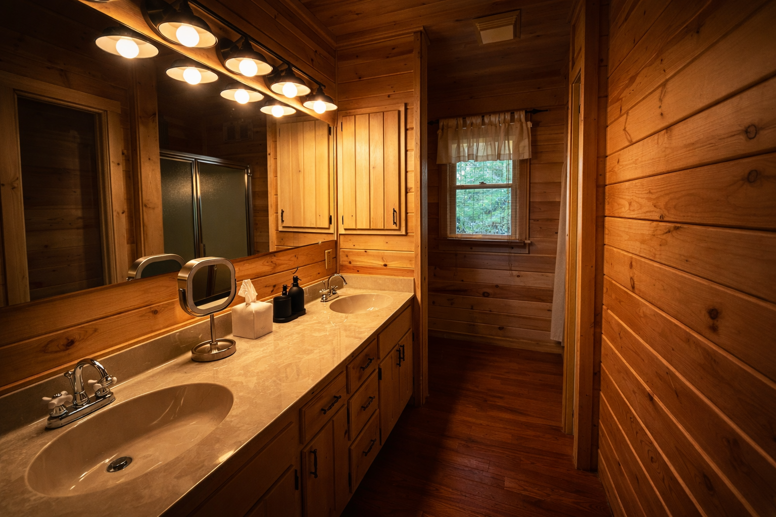 Wood-paneled bathroom with double sink vanity, large mirror, and window showing trees outside.