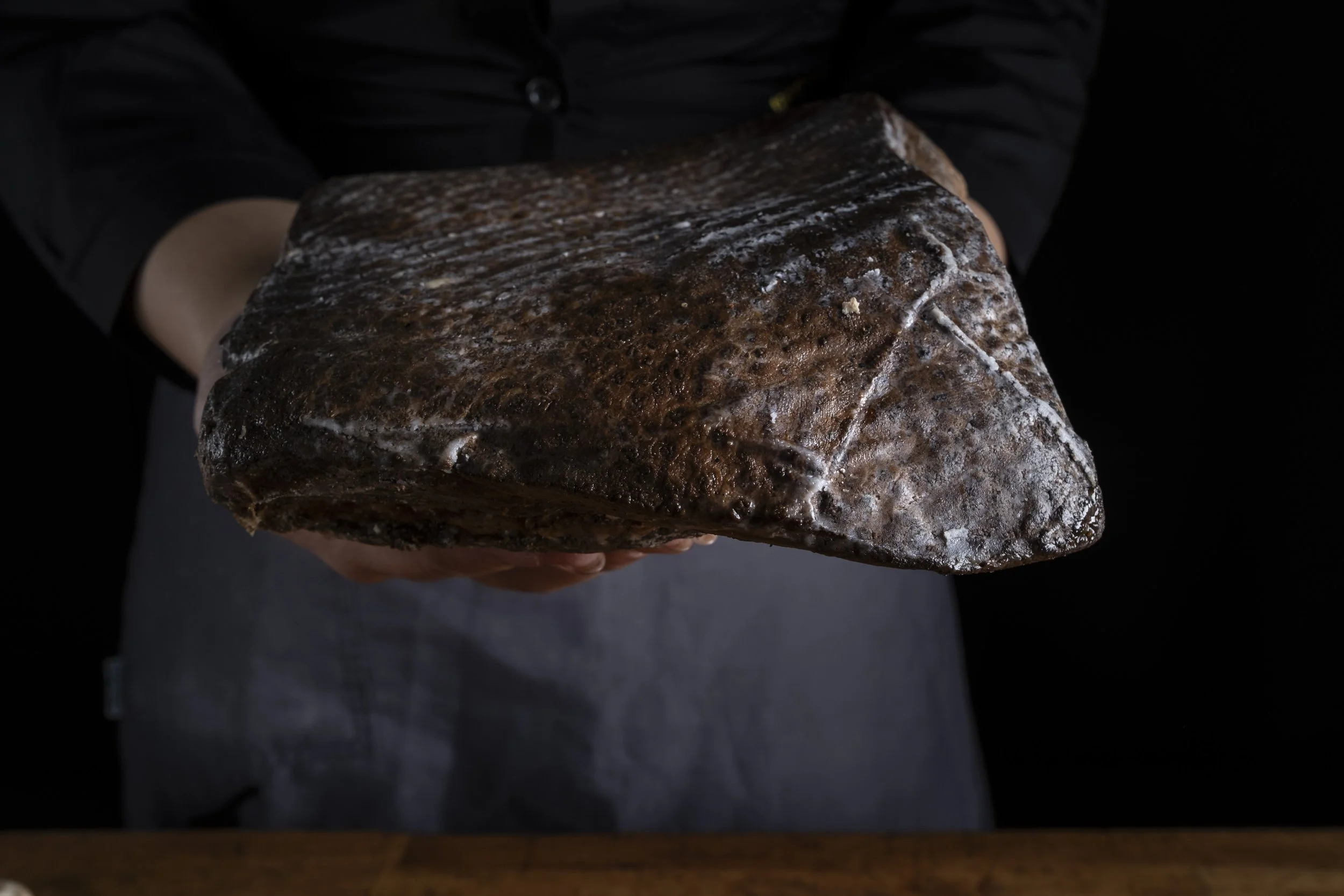 Un mano che tiene un masso di roccia scura su uno sfondo nero.