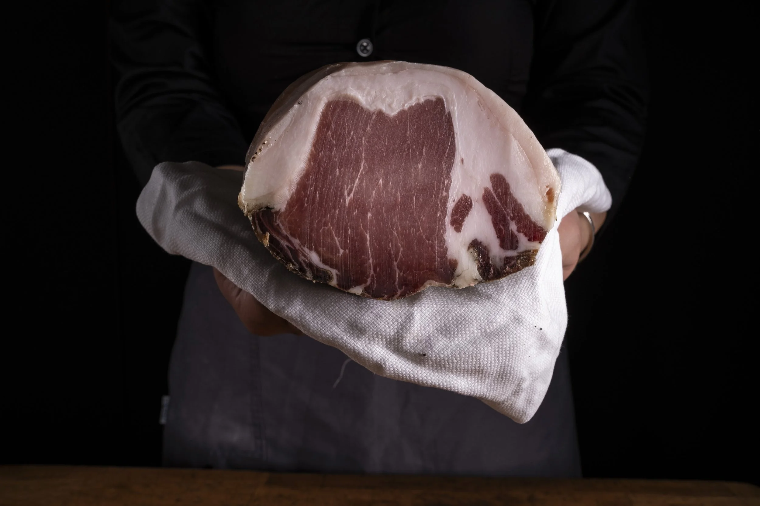 Una persona tiene in mano un pez con carne rosata e una pelle bianca, avvolto in un panno bianco, contro uno sfondo nero.