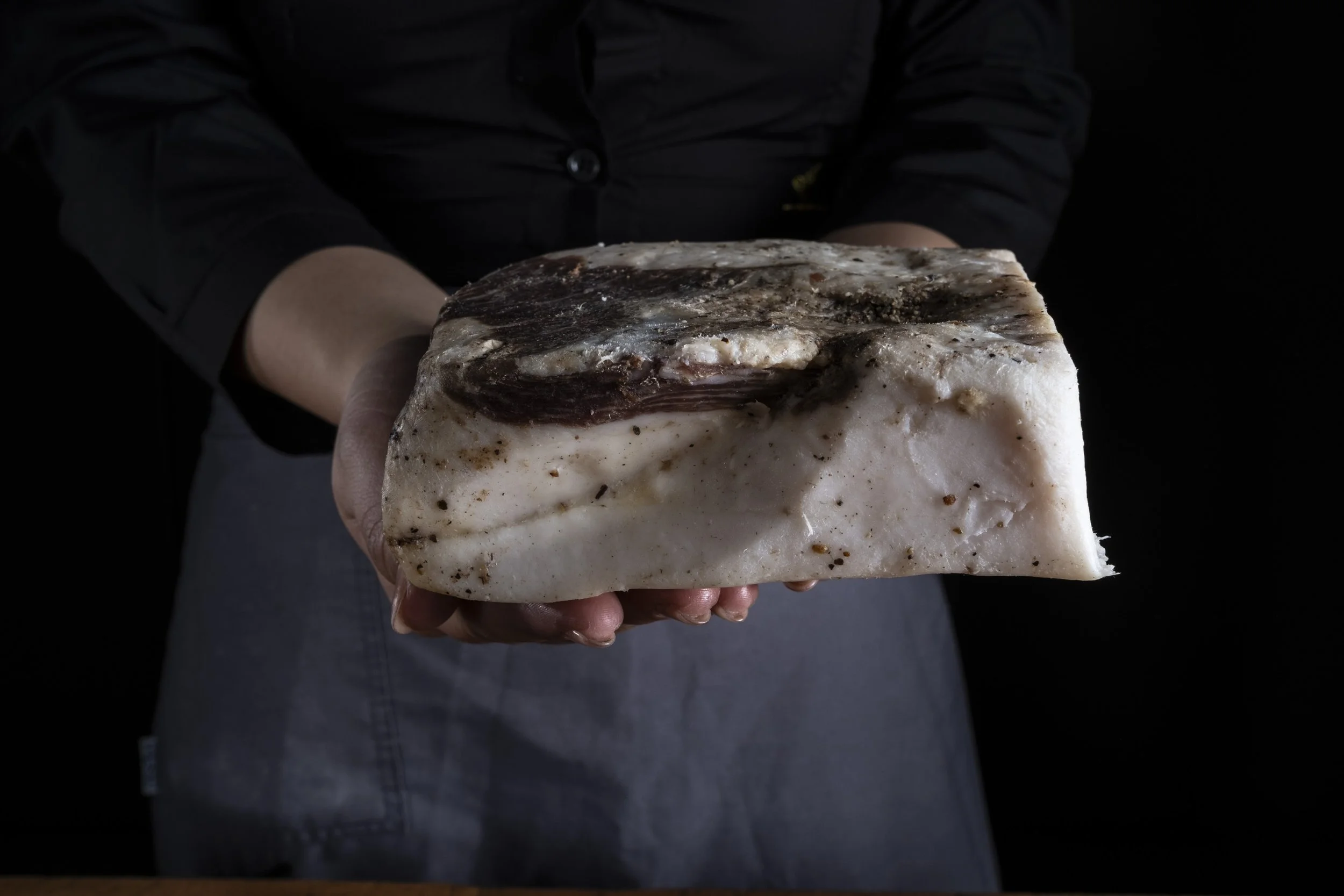 Persona che tiene un blocco di sale grosso con pepe e altre spezie visibili.