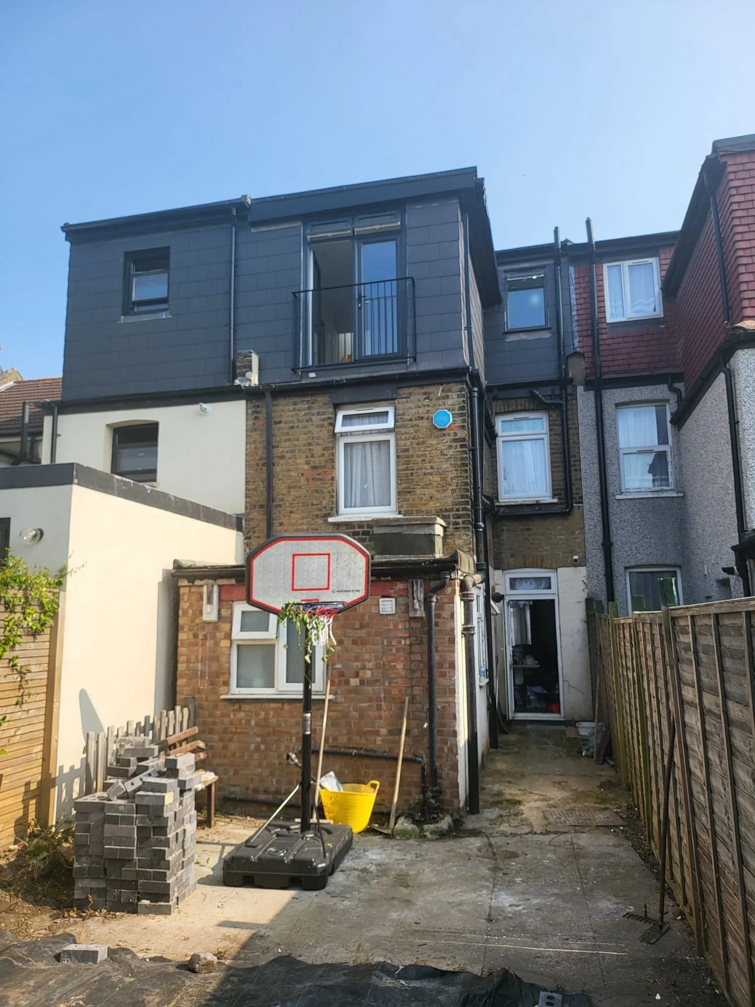 Backyard of a house with a basketball hoop, a stack of bricks, and construction materials.