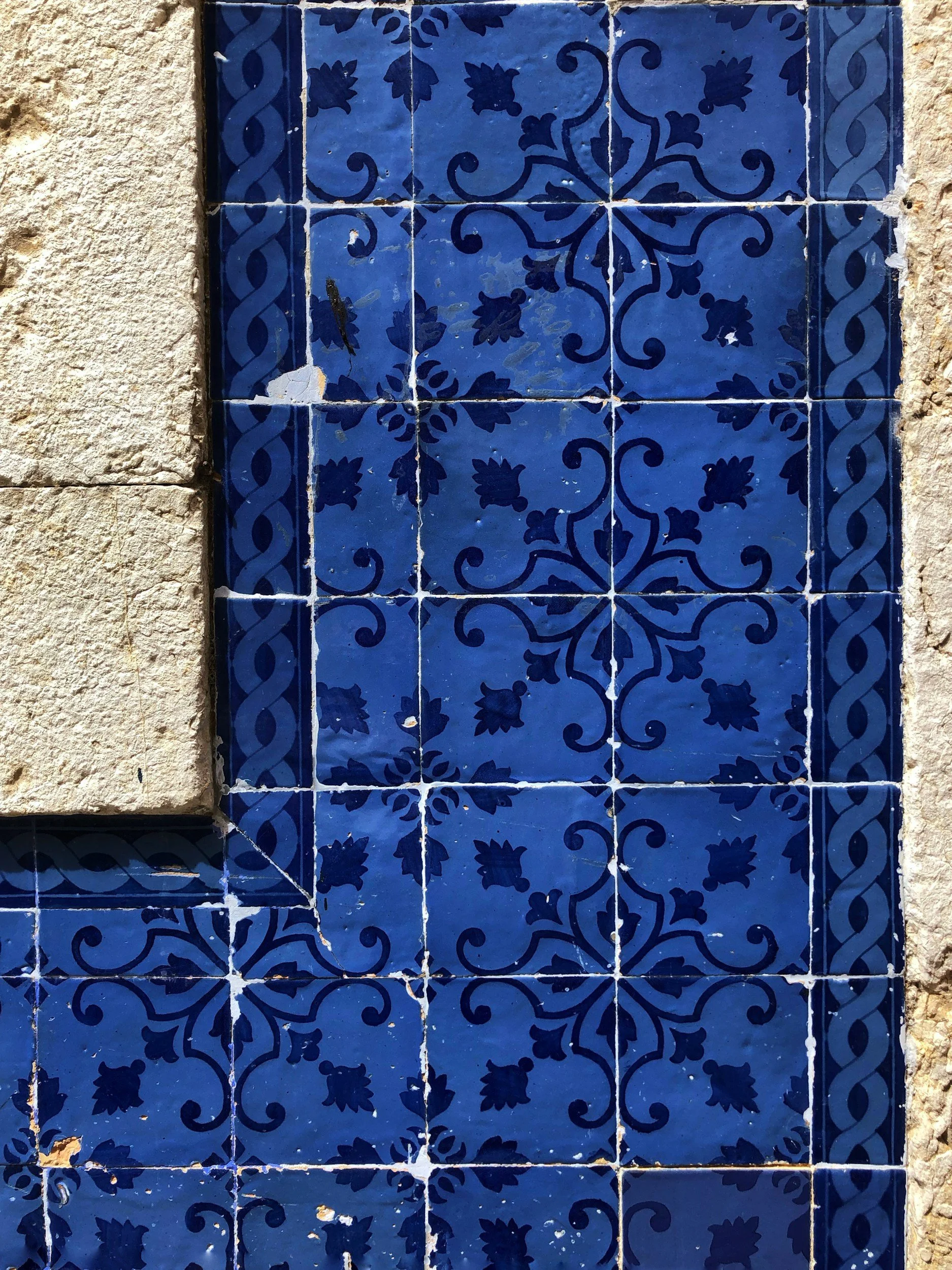 Close-up of a decorative blue ceramic tile wall with intricate floral and geometric patterns, surrounded by rough stone and plaster.