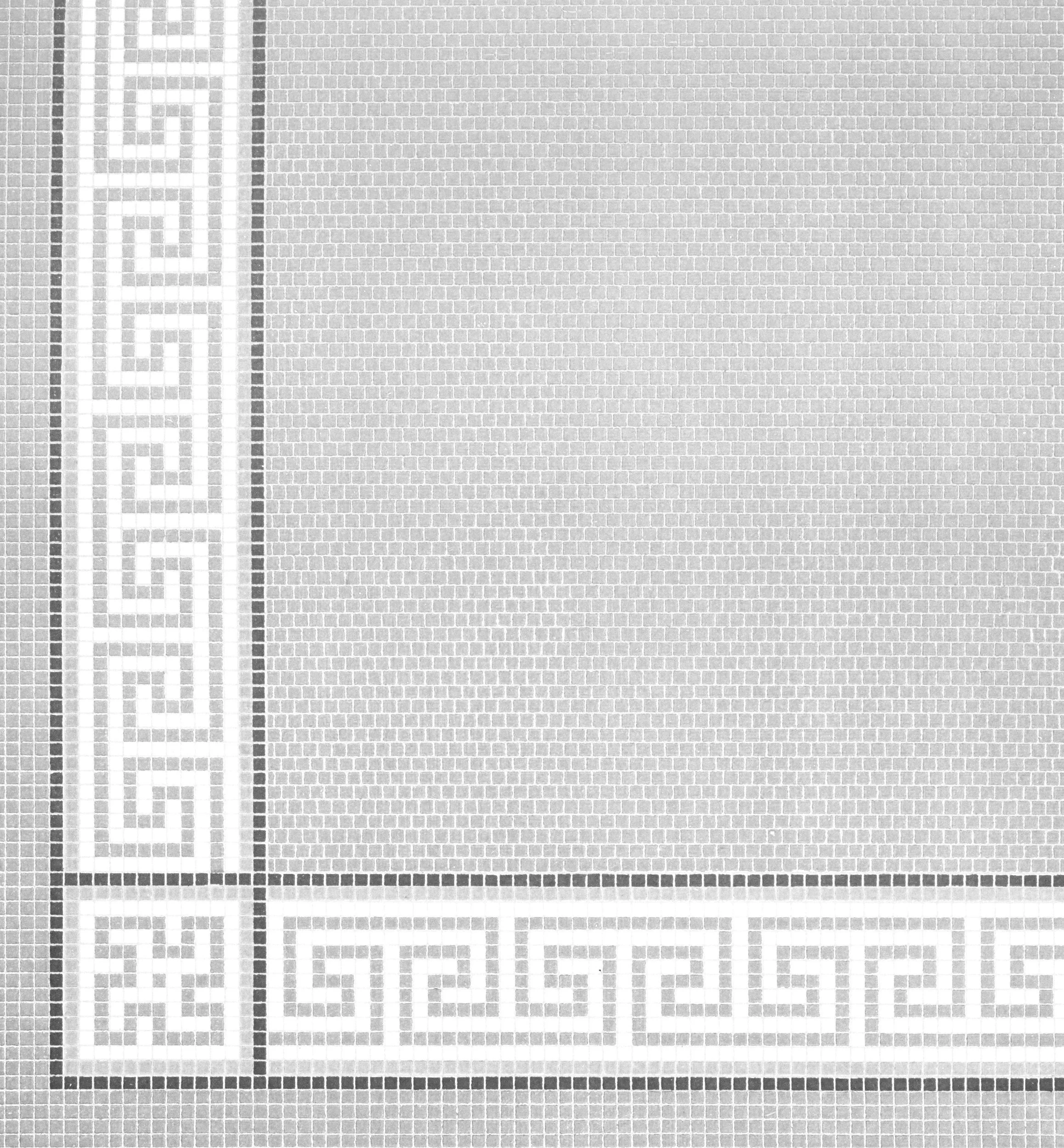 Close-up of a mosaic tile pattern with a Greek key design in white and gray.