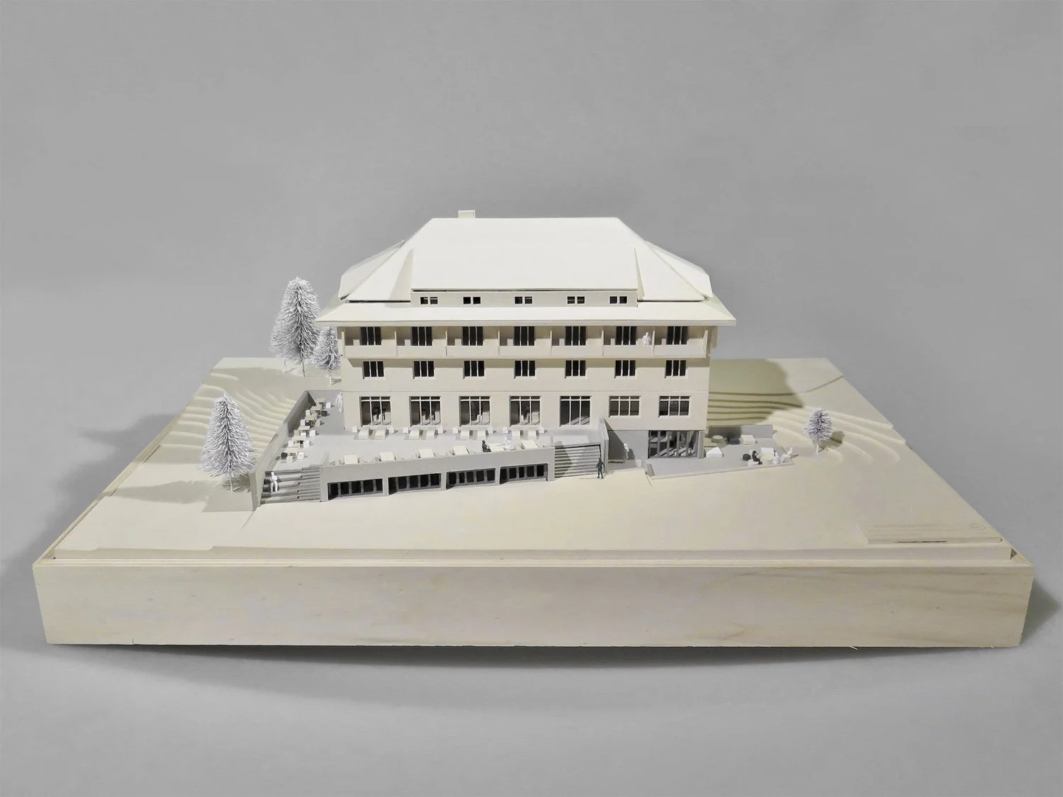 Architectural model of a multi-story building with balconies, a terrace, and surrounding trees on a wooden base.