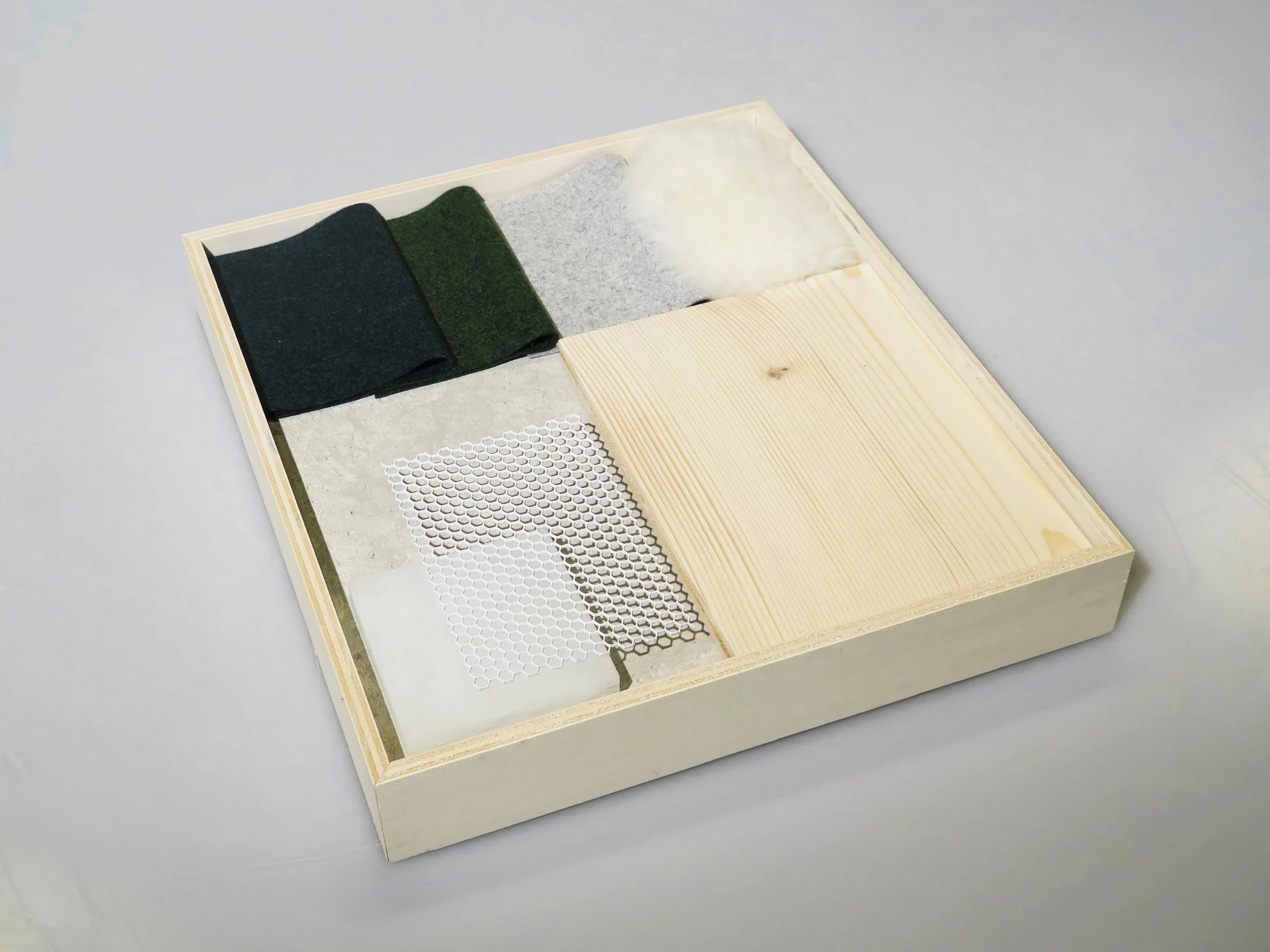 A wooden box containing various textured materials including felt cloth, cotton, mesh, and paper samples.