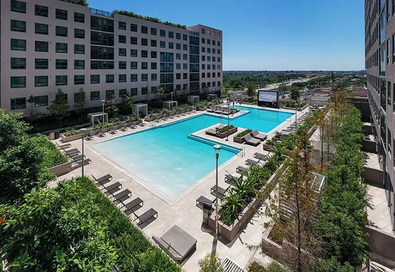 The One at University City by Landmark Properties – a swimming pool in an urban setting, surrounded by lounge chairs, greenery, and high-rise buildings, under a clear blue sky.
