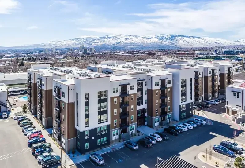 Saga Reno by Landmark Properties – modern apartment complex with parked cars in a lot, snow-capped mountains in the background, clear sky.