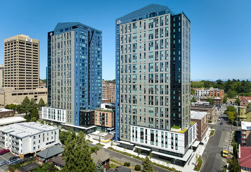 The Standard at Seattle by Landmark Properties – two tall modern high-rise buildings with glass facades in an urban area, with smaller buildings and streets in the foreground and a blue sky in the background.