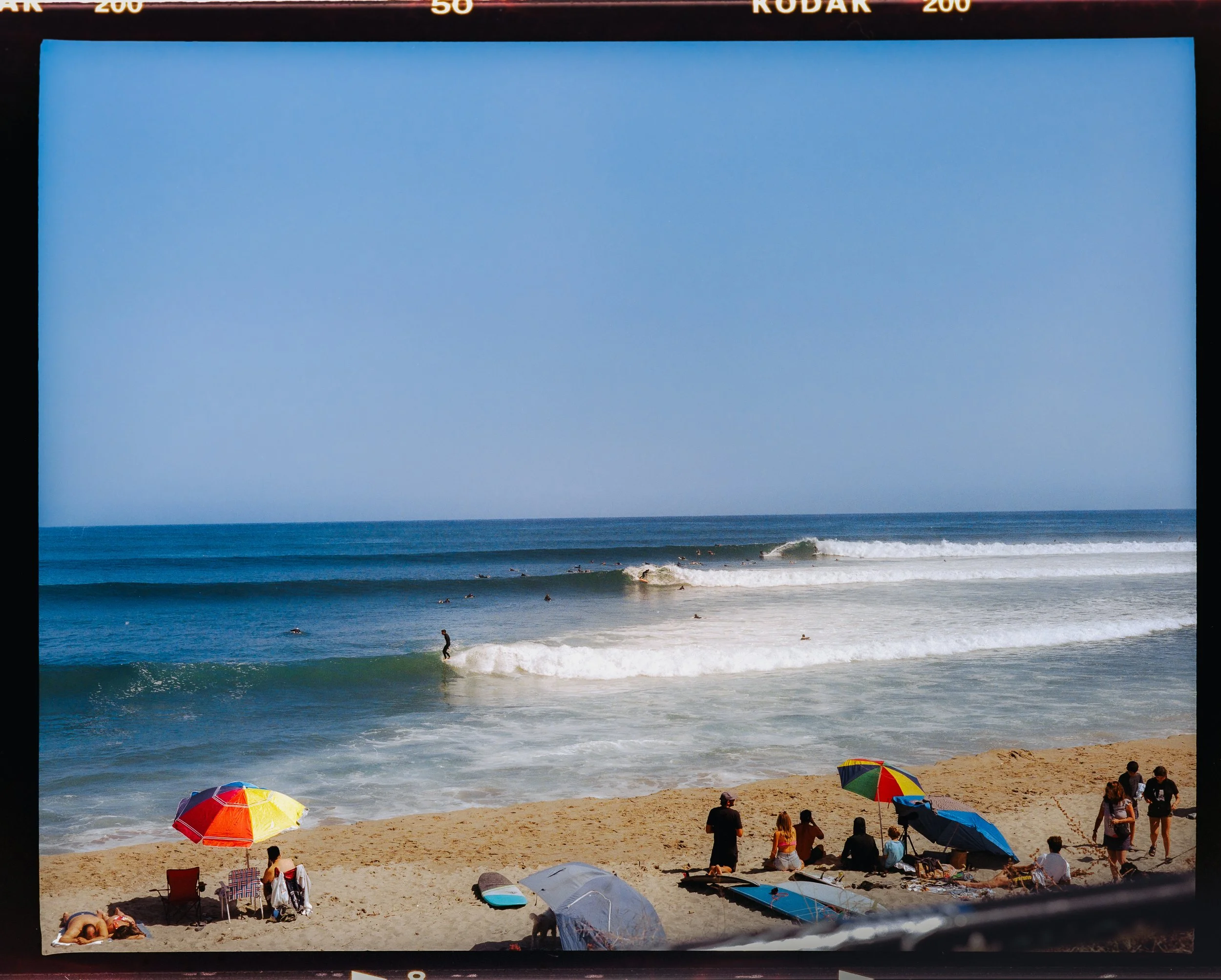 A view of the ocean as surfers catch waves and sunbathers at the beach in the foreground
