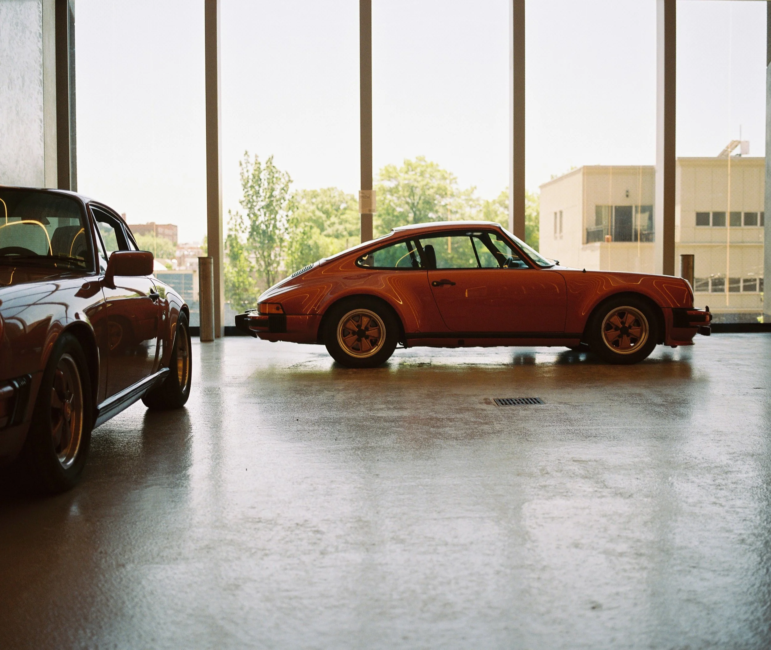 A film photoraphy view of two brown Porsches with a glass window backdrop
