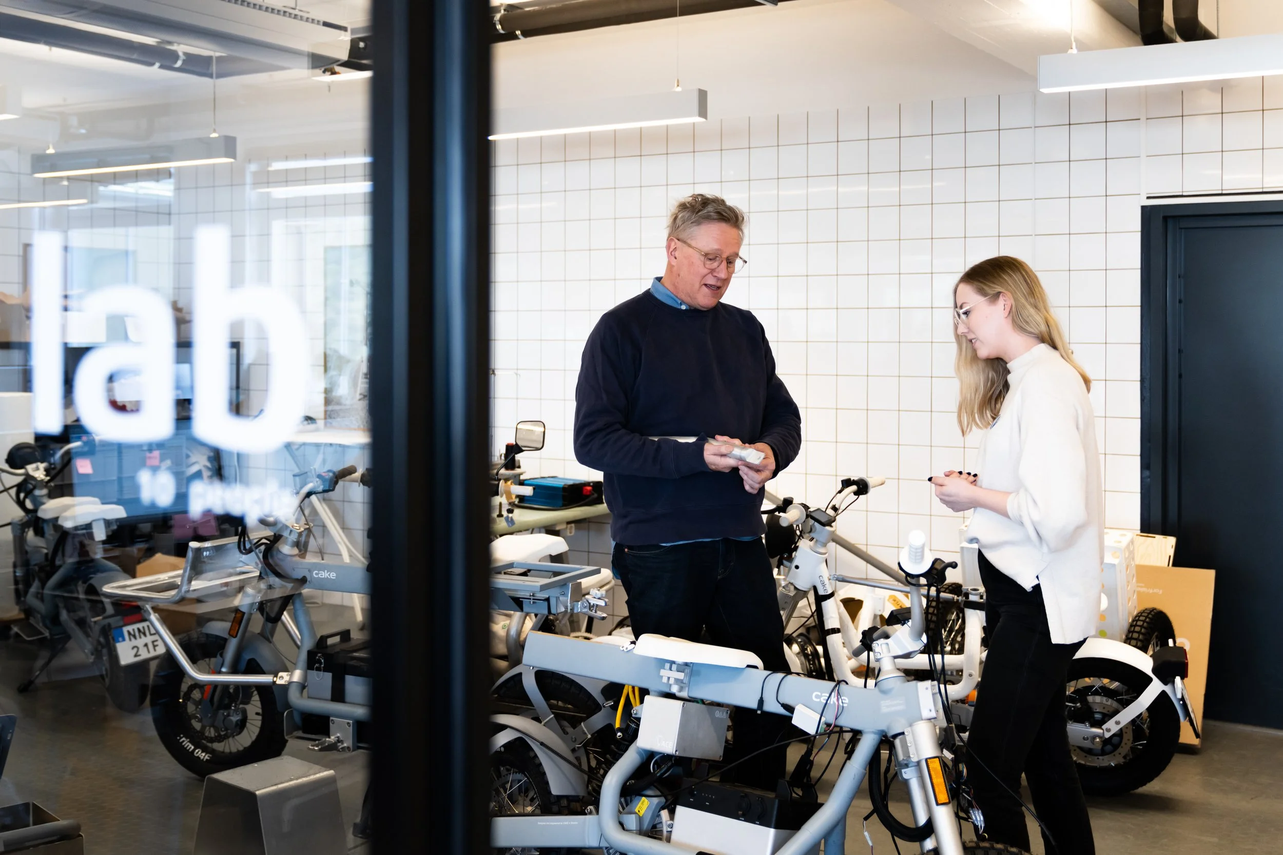 Stefan Ytterborn with one of his team members discussing something. They are standing in front of a CAKE motorcycle and have a number of motorcycles in the room.